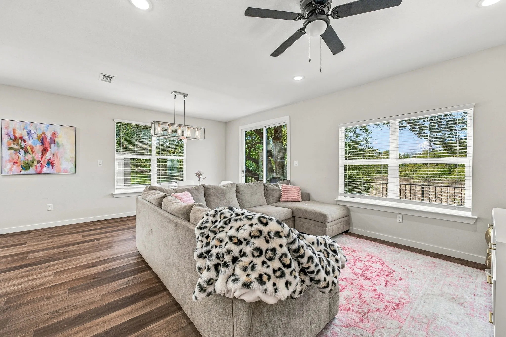 Open-concept space featuring wood-finish flooring, recessed lighting, a modern ceiling fan, and multiple large windows with natural light