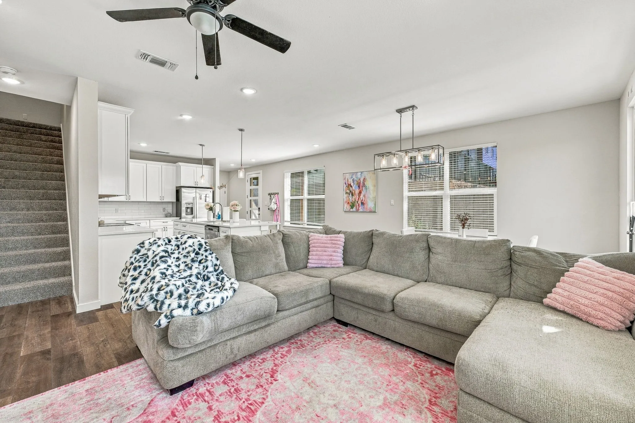 Open-concept living space featuring wood-finish flooring, a kitchen with white cabinetry, a center island with pendant lighting, and multiple windows