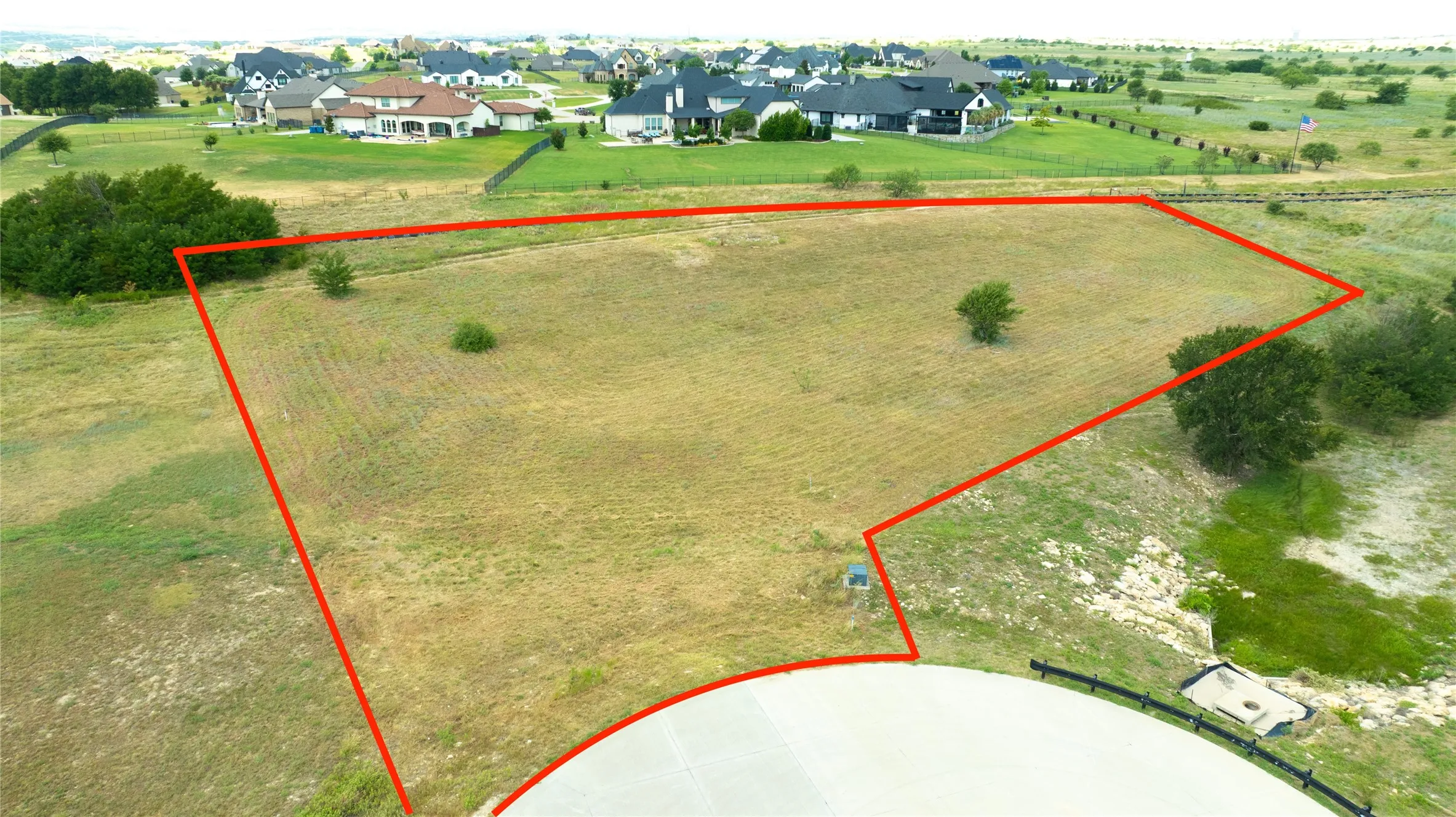 Expansive cleared lot featuring mature trees and a paved concrete driveway entry
