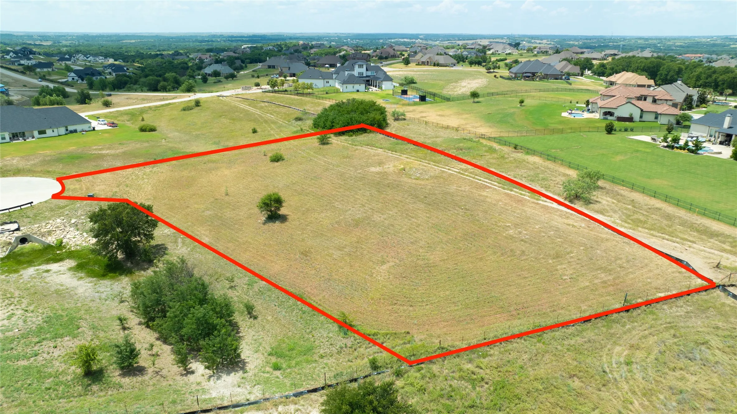 Expansive, cleared lot featuring open terrain, established perimeter fencing, mature trees, and access to a paved cul-de-sac