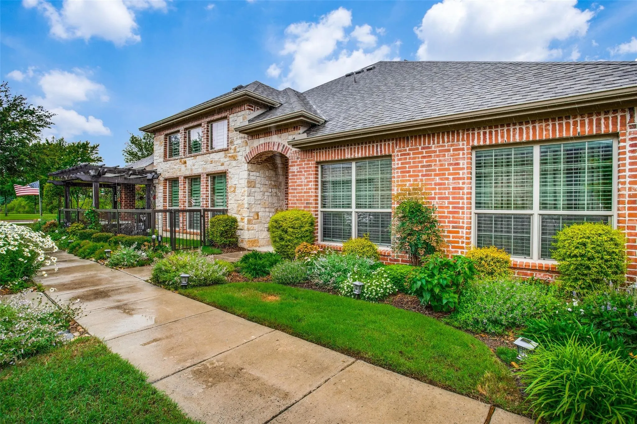 Brick and stone veneer exterior featuring a concrete walkway, multi-pane windows, and a detached wooden pergola