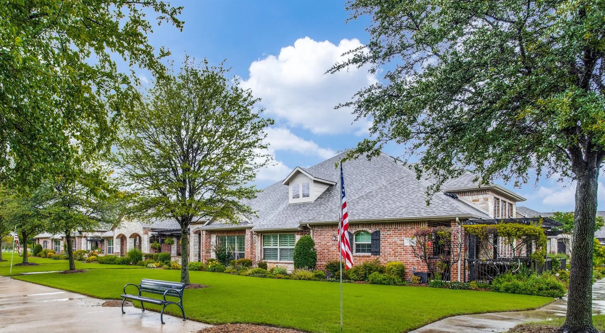 Brick exterior with stone accents, architectural shingle roof, dormer window, and mature landscaping