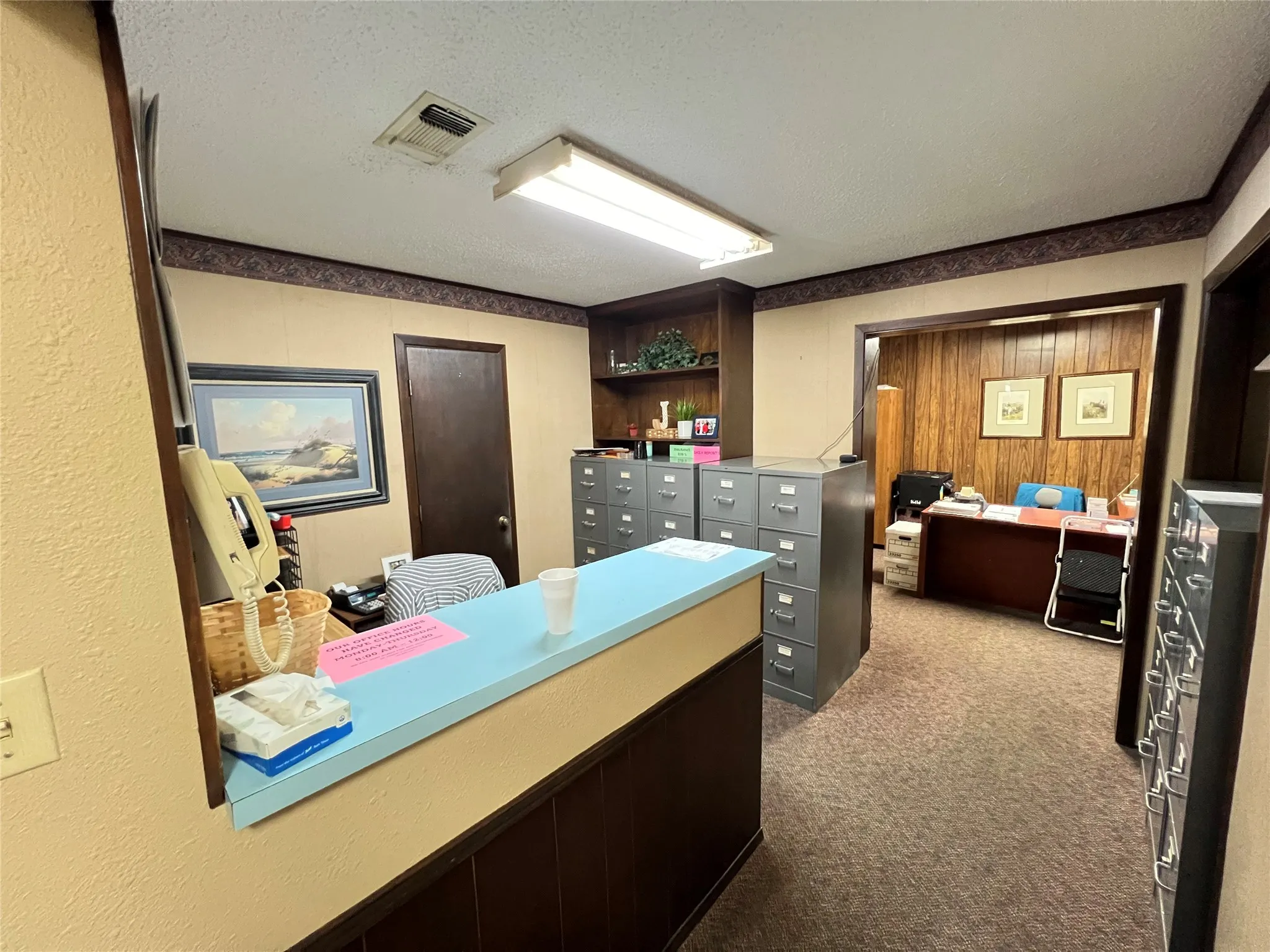 Built-in reception counter with laminate surface, integrated floor-to-ceiling wooden shelving, and dark-finished wooden door