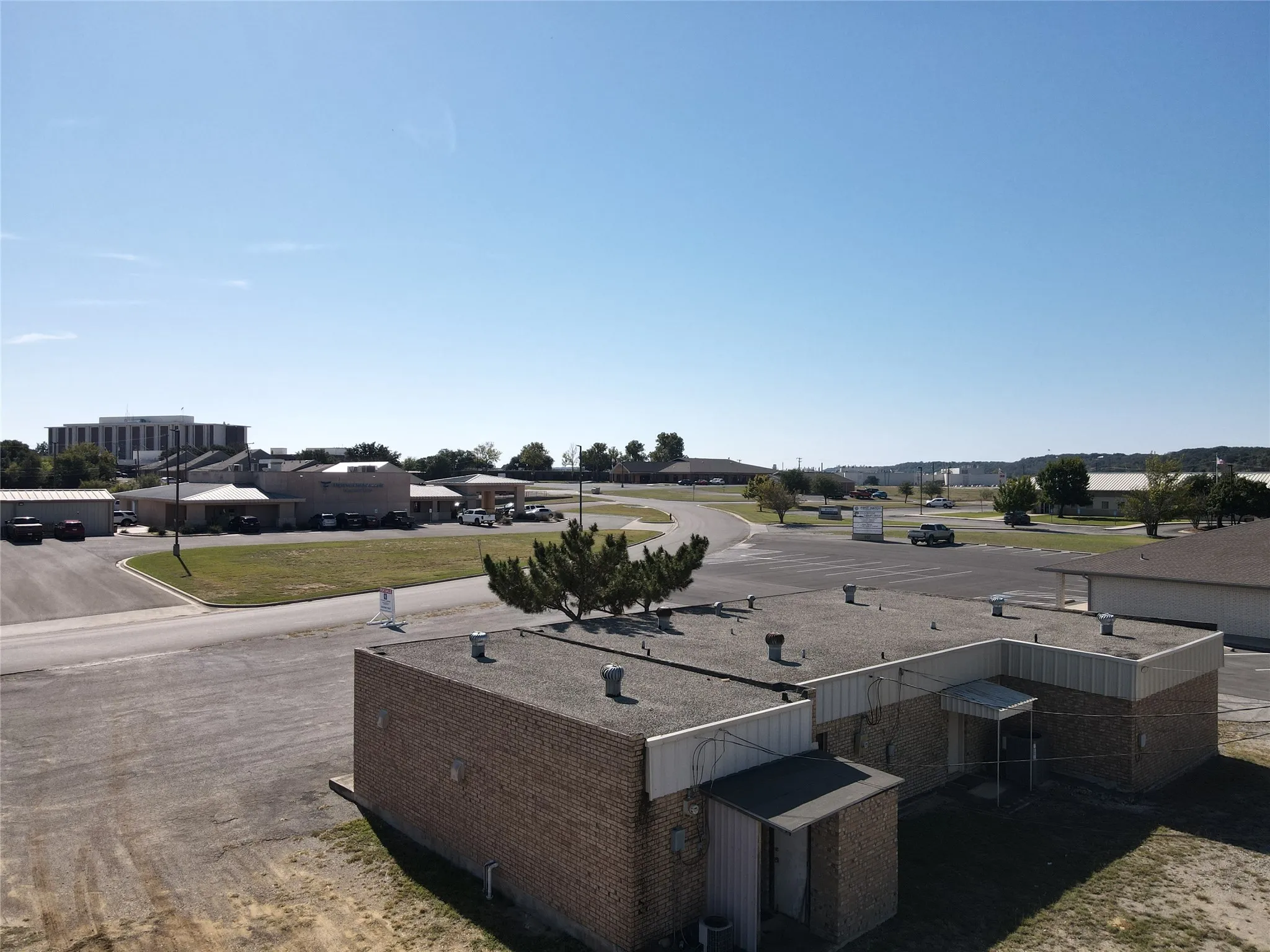 Single-story masonry structure with a flat roof, featuring an expansive exterior lot with paved parking area and direct road access
