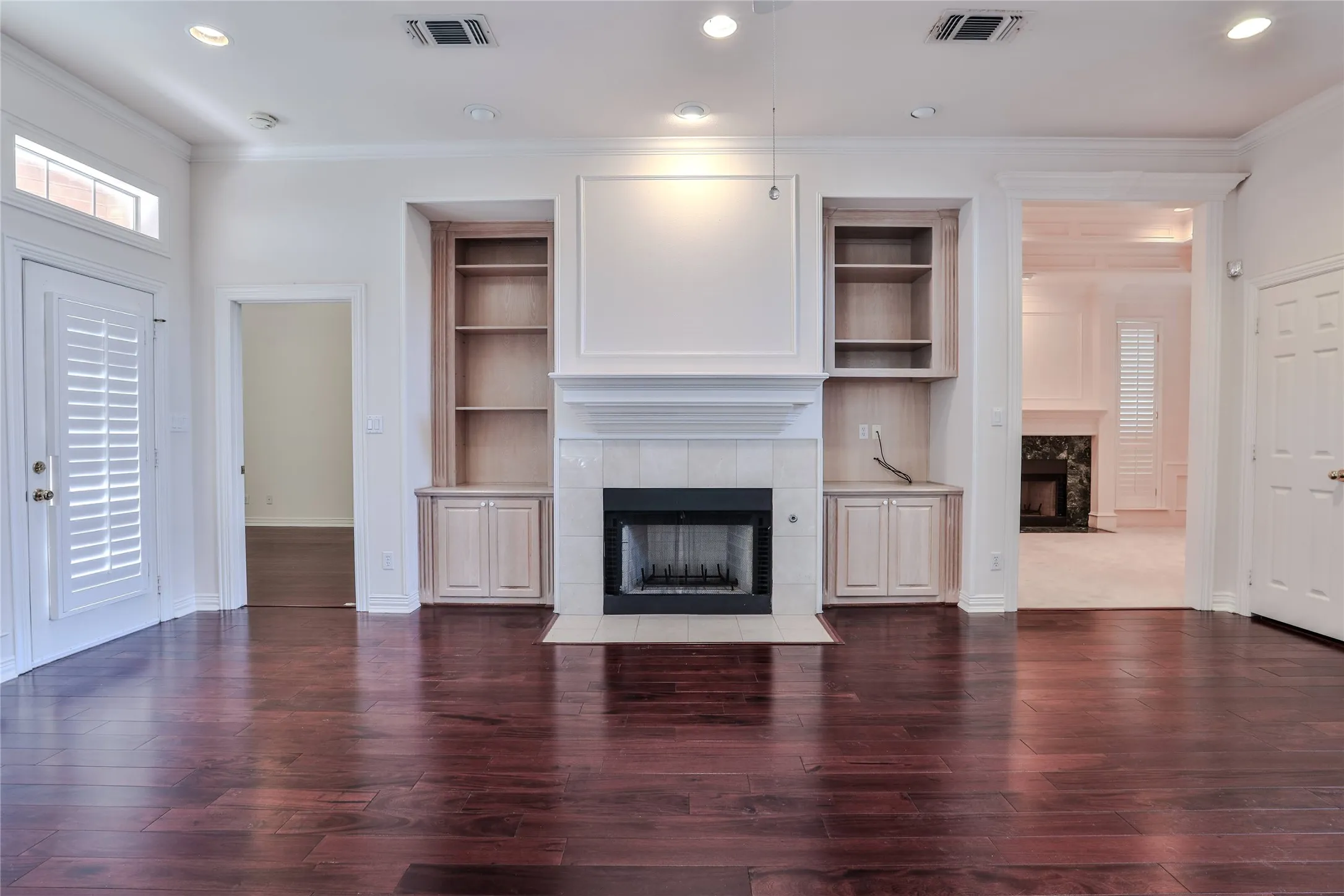 Wood-finish flooring, fireplace with a tile surround, recessed lighting, and custom built-in cabinetry featuring integrated shelving