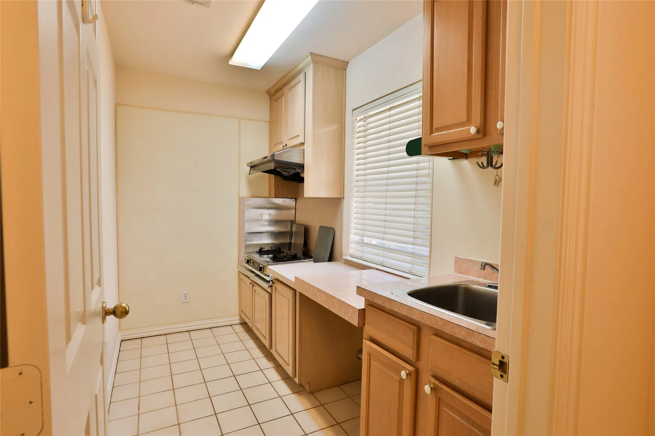 Kitchen featuring light wood-finish cabinetry, tile flooring, integrated cooktop, stainless steel sink, and solid-surface countertops