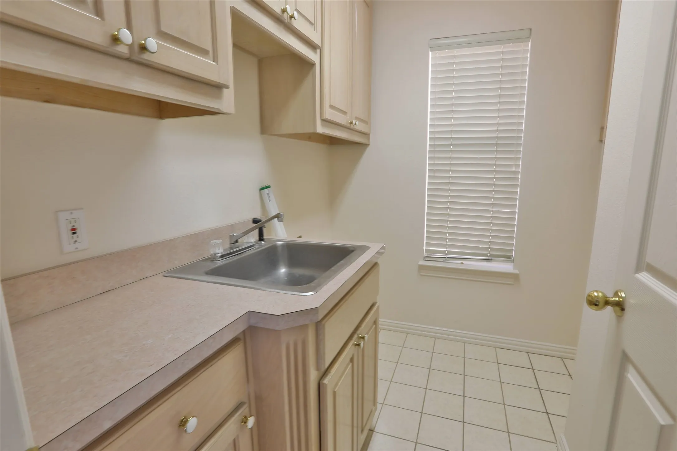 Utility area featuring light-finish cabinetry, solid-surface countertop, stainless steel drop-in sink with a chrome faucet, and ceramic tile flooring