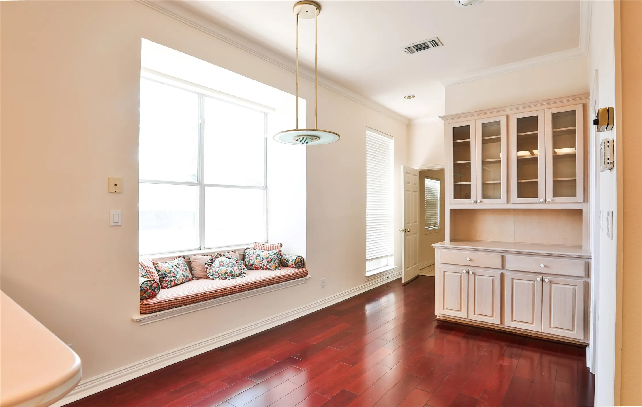 Wood-finish flooring, built-in floor-to-ceiling cabinetry with glass-front uppers, and a recessed window seat featuring a large-pane window and pendant lighting
