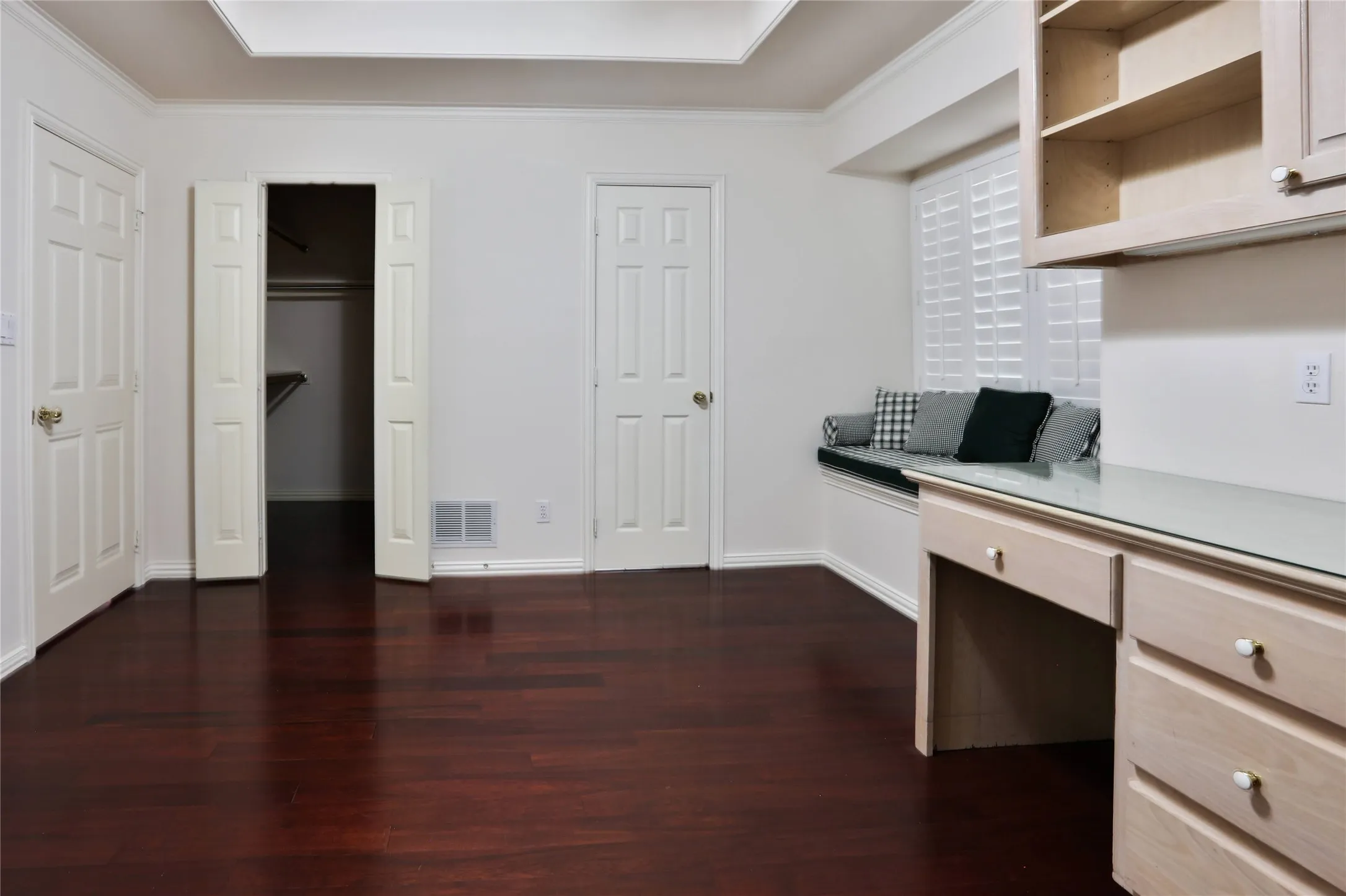 Wood-finish flooring, tray ceiling, built-in desk with overhead cabinetry, and integrated window seating featuring plantation shutters