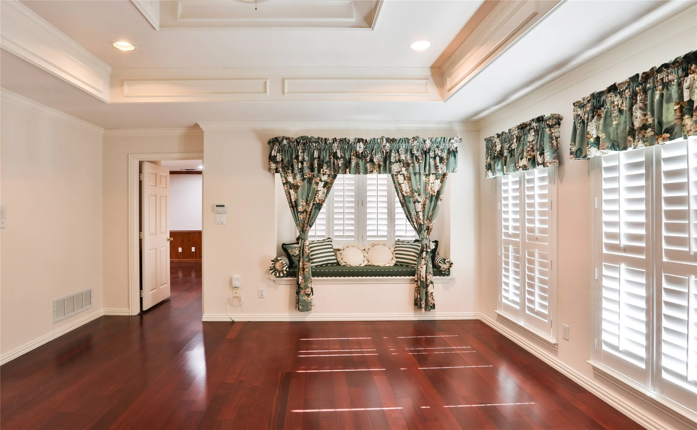Coffered ceiling with recessed lighting, integrated window seat, wood-finish flooring, and white plantation shutters