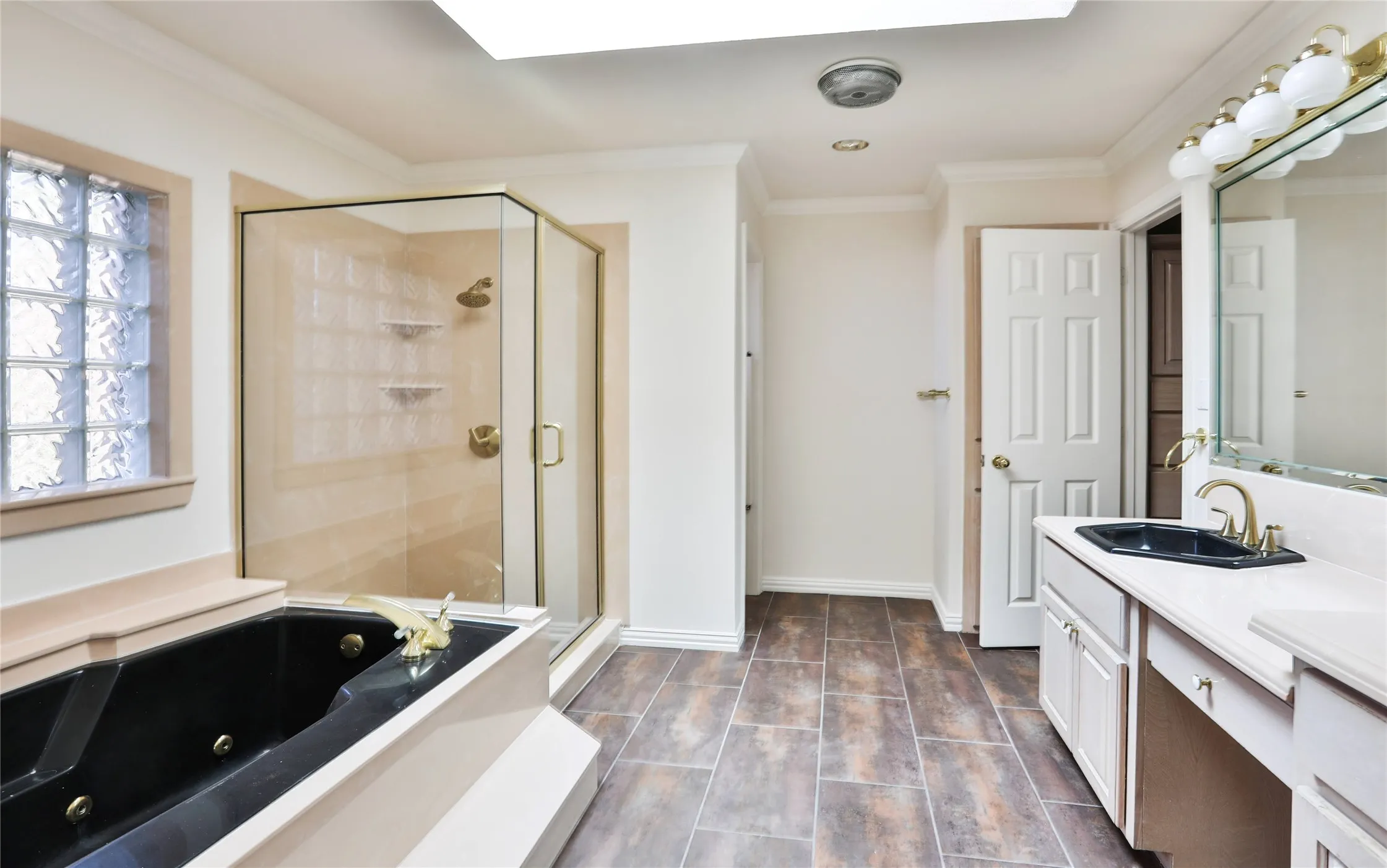 Bathroom featuring a jetted bathtub, separate glass-enclosed shower, dual-tone vanity with a dark-finish sink, glass block window, and tile flooring
