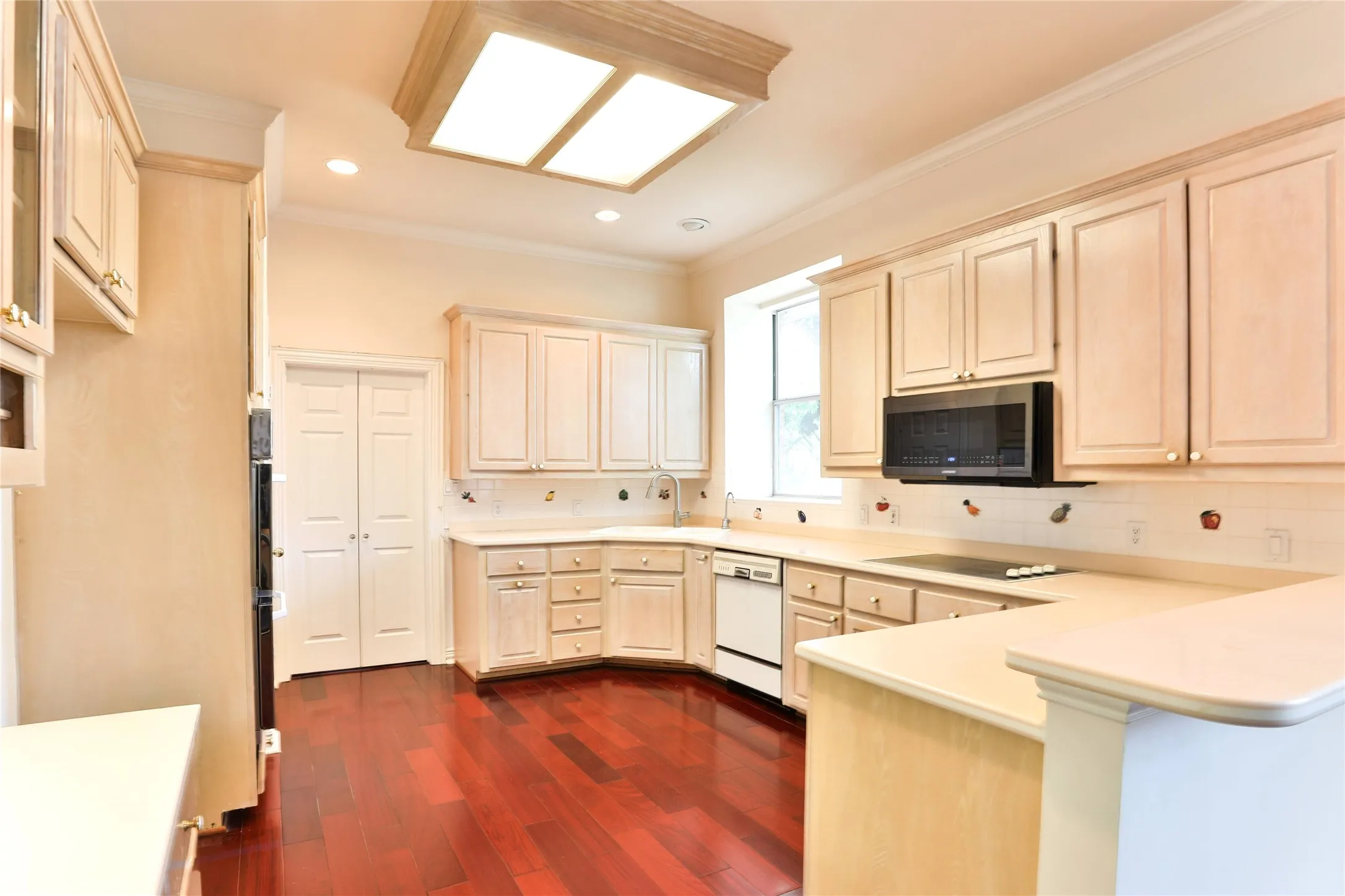 Kitchen featuring light-finish wood cabinetry, wood-finish flooring, solid-surface countertops, built-in microwave, and recessed lighting