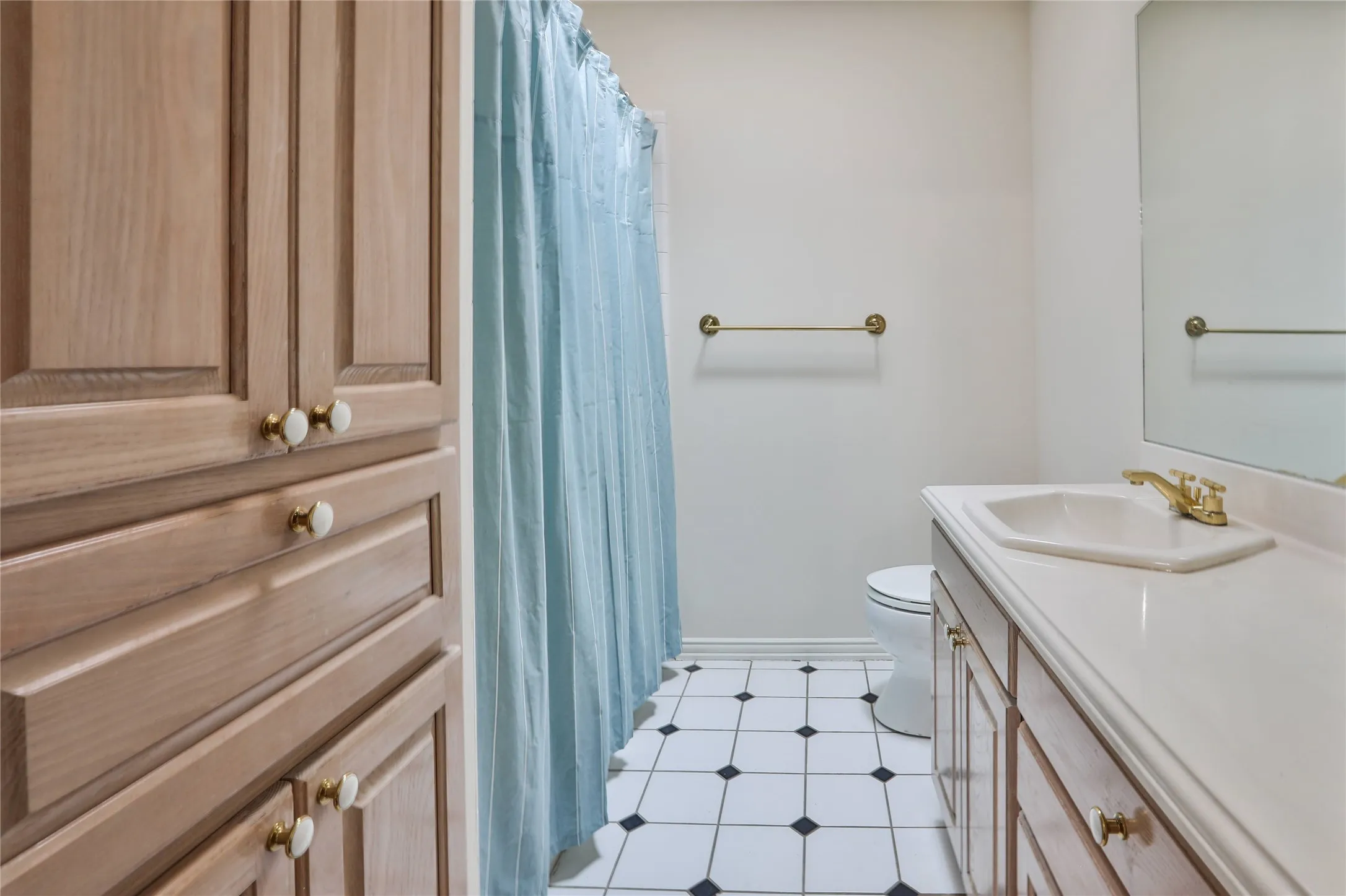 Bathroom featuring wood-finish cabinetry, a white vanity countertop with an integrated basin, brass-toned hardware, and a monochrome tile floor