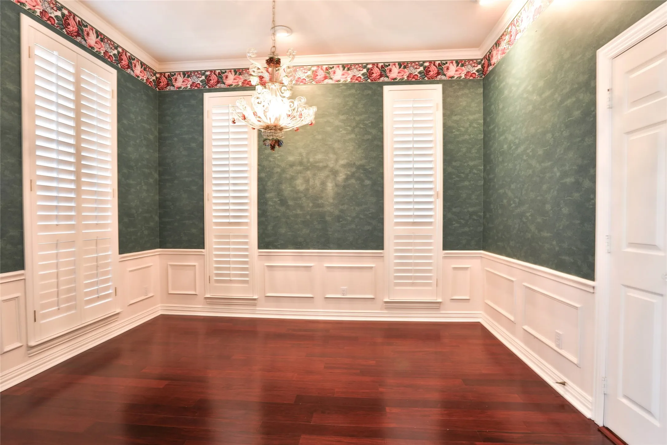 Formal room featuring wood-finish flooring, white plantation shutters, decorative wall molding, and a traditional multi-light chandelier