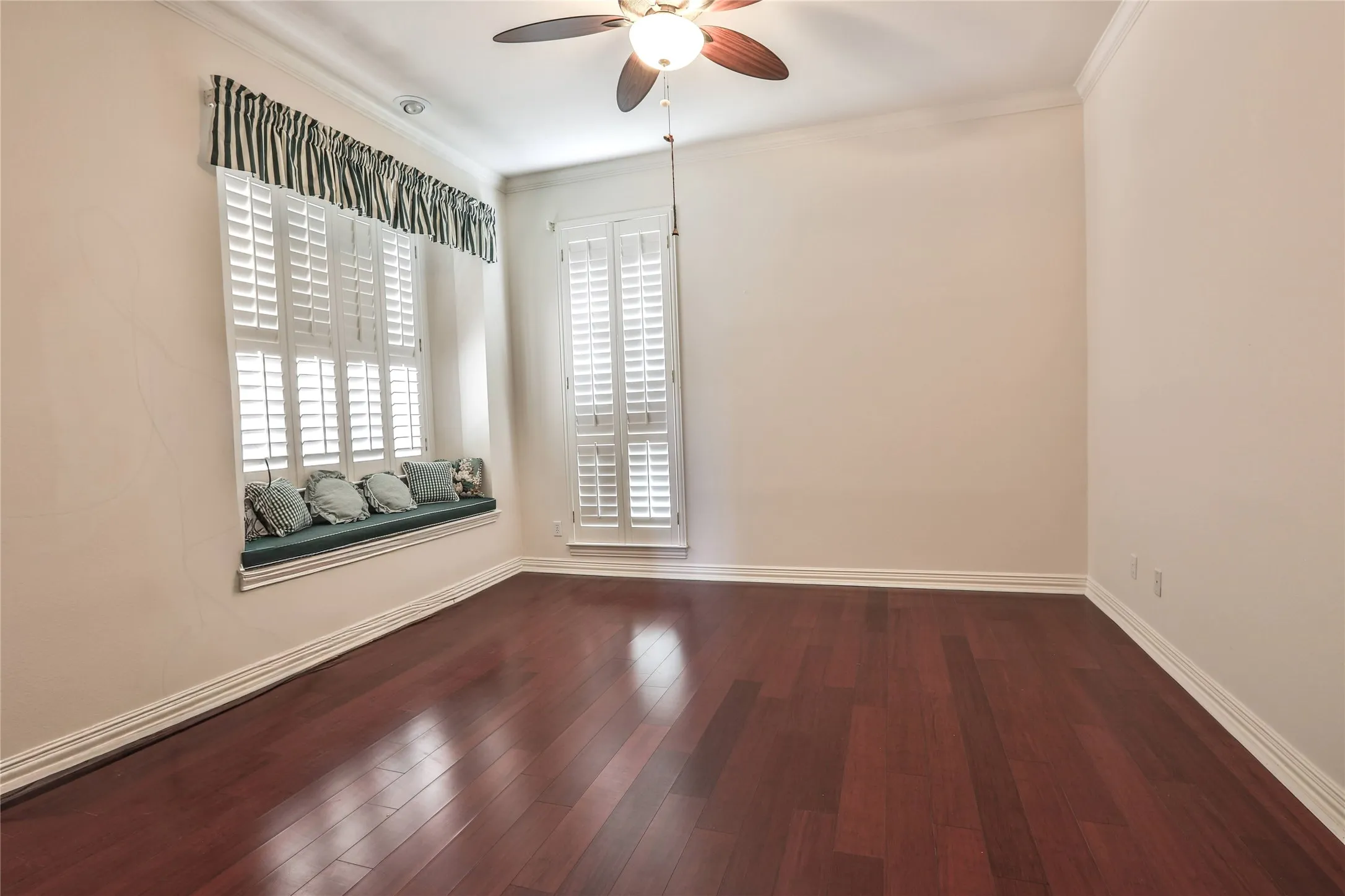 Room featuring wood-finish flooring, built-in window seating, plantation shutters, and a ceiling fan