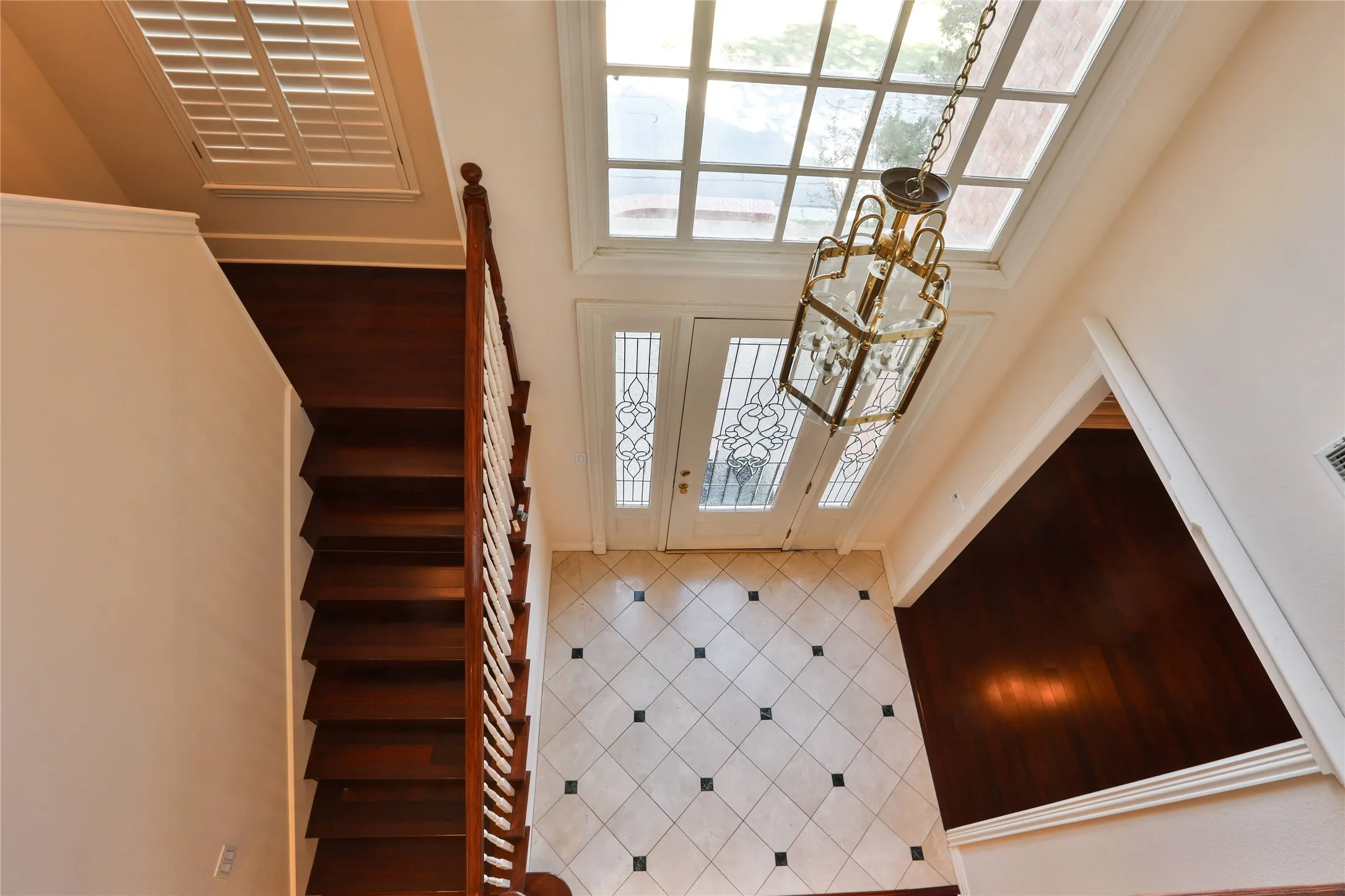Foyer featuring tile flooring with decorative inserts, wood-finish staircase with white balusters, multi-pane transom window, and a multi-tiered metal chandelier