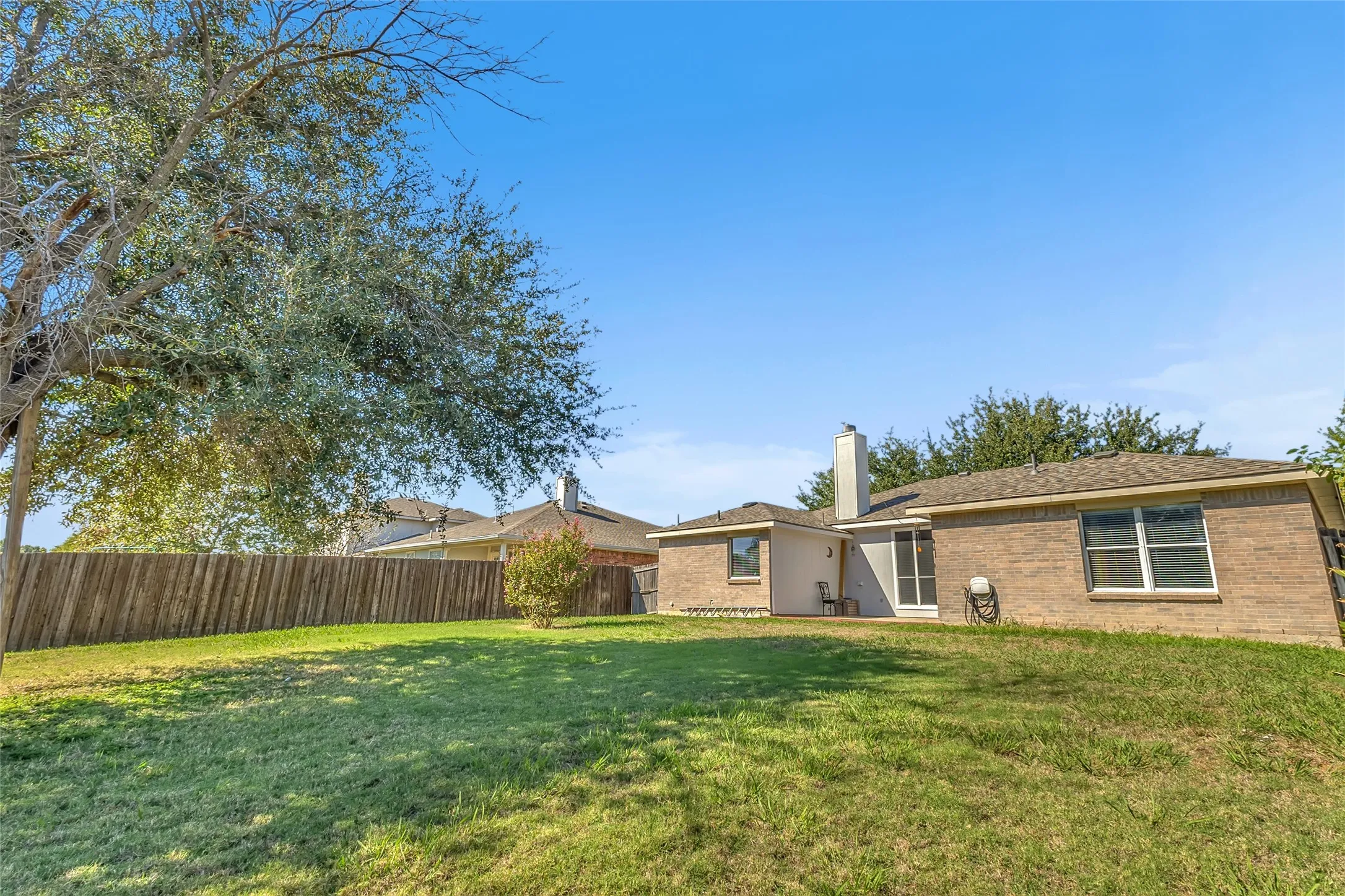 Fenced backyard with lawn, mature tree, and rear patio access