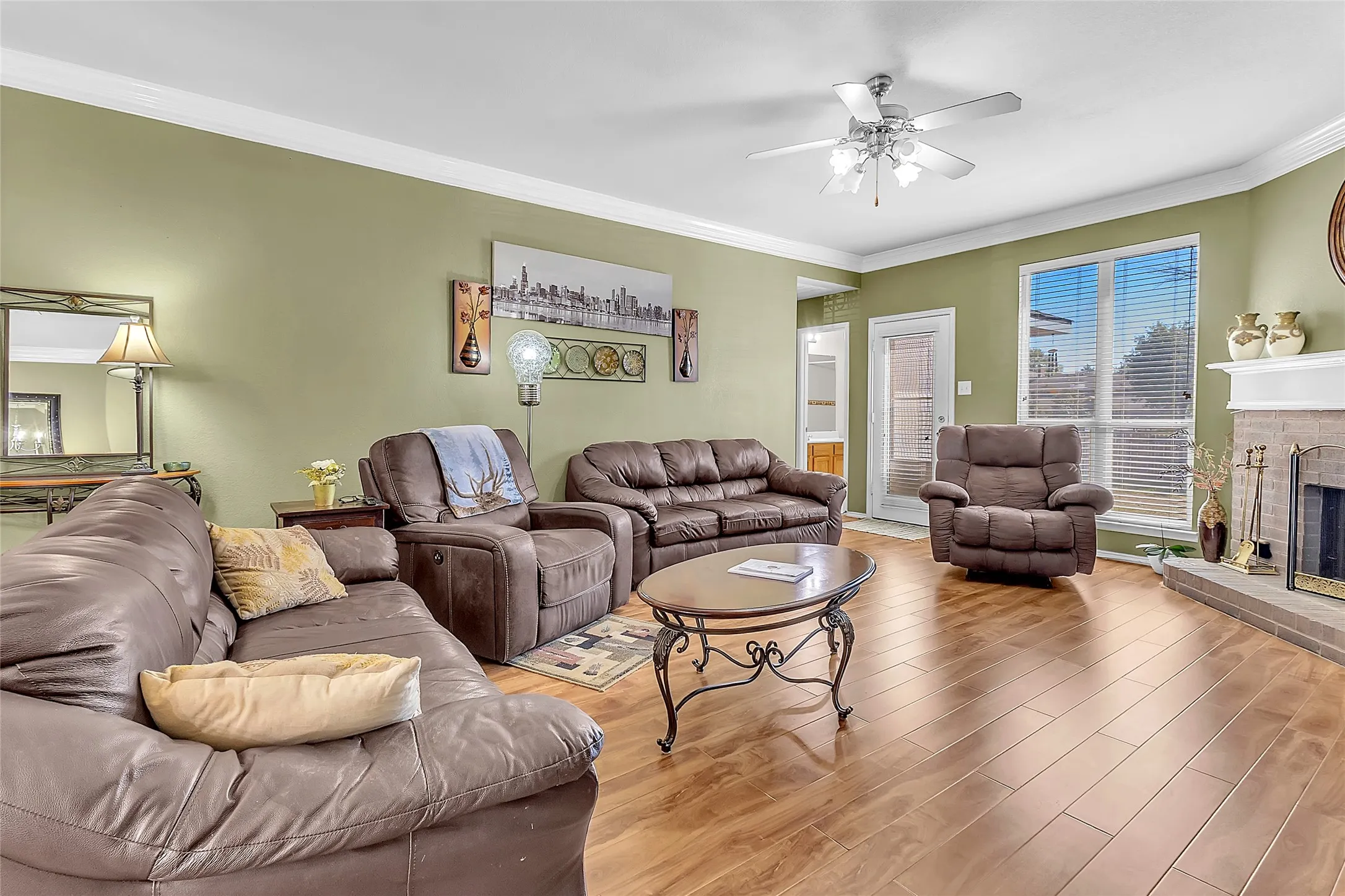 Living room with brick fireplace, manufactured-wood floors, and ceiling fan — Denton