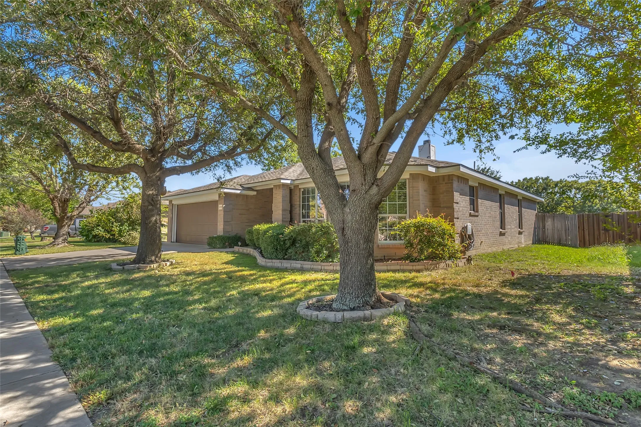 Street view: single-story brick home, attached garage, mature trees