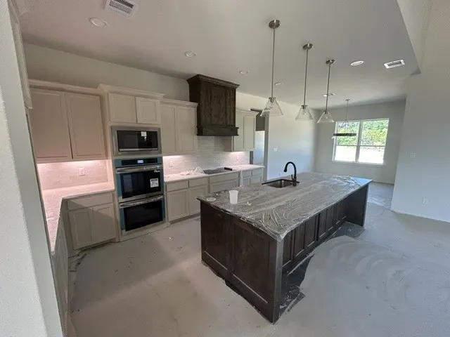 Kitchen featuring off-white cabinetry, a dark wood-finish center island, stone-surface countertops, built-in double wall ovens, and pendant lighting