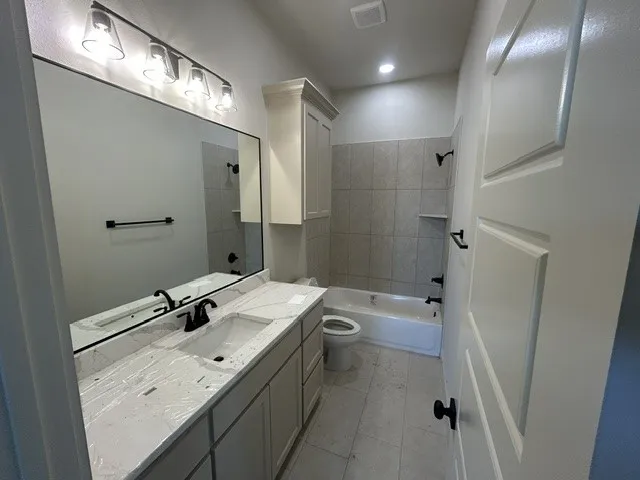 Bathroom featuring vanity with stone-look countertop, undermount sink, matte black hardware, built-in upper cabinetry, and tiled shower-tub combination