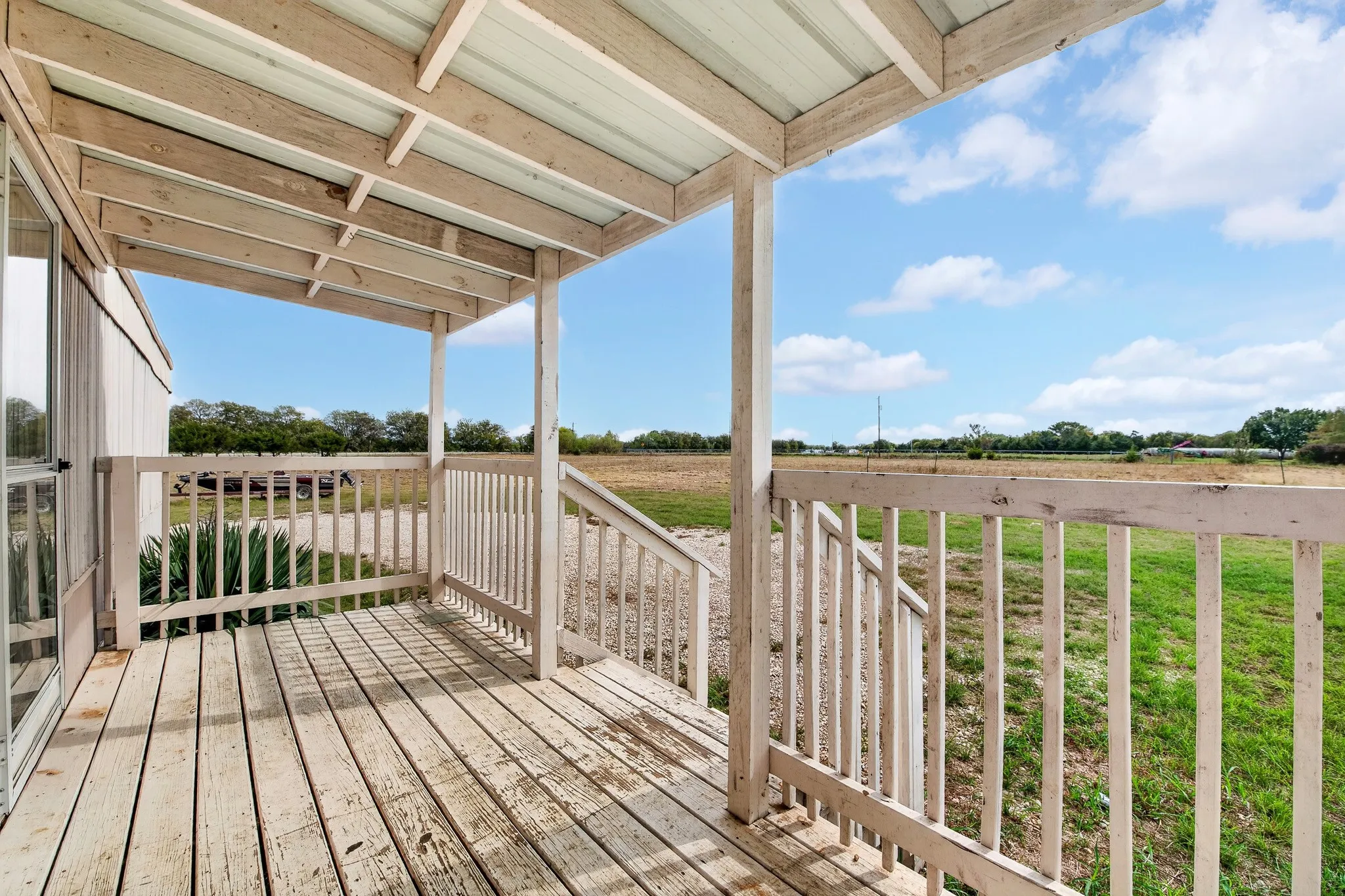 Covered wood deck featuring a protective roof overhang, painted wooden balustrade, and staircase leading to a grass-covered lot