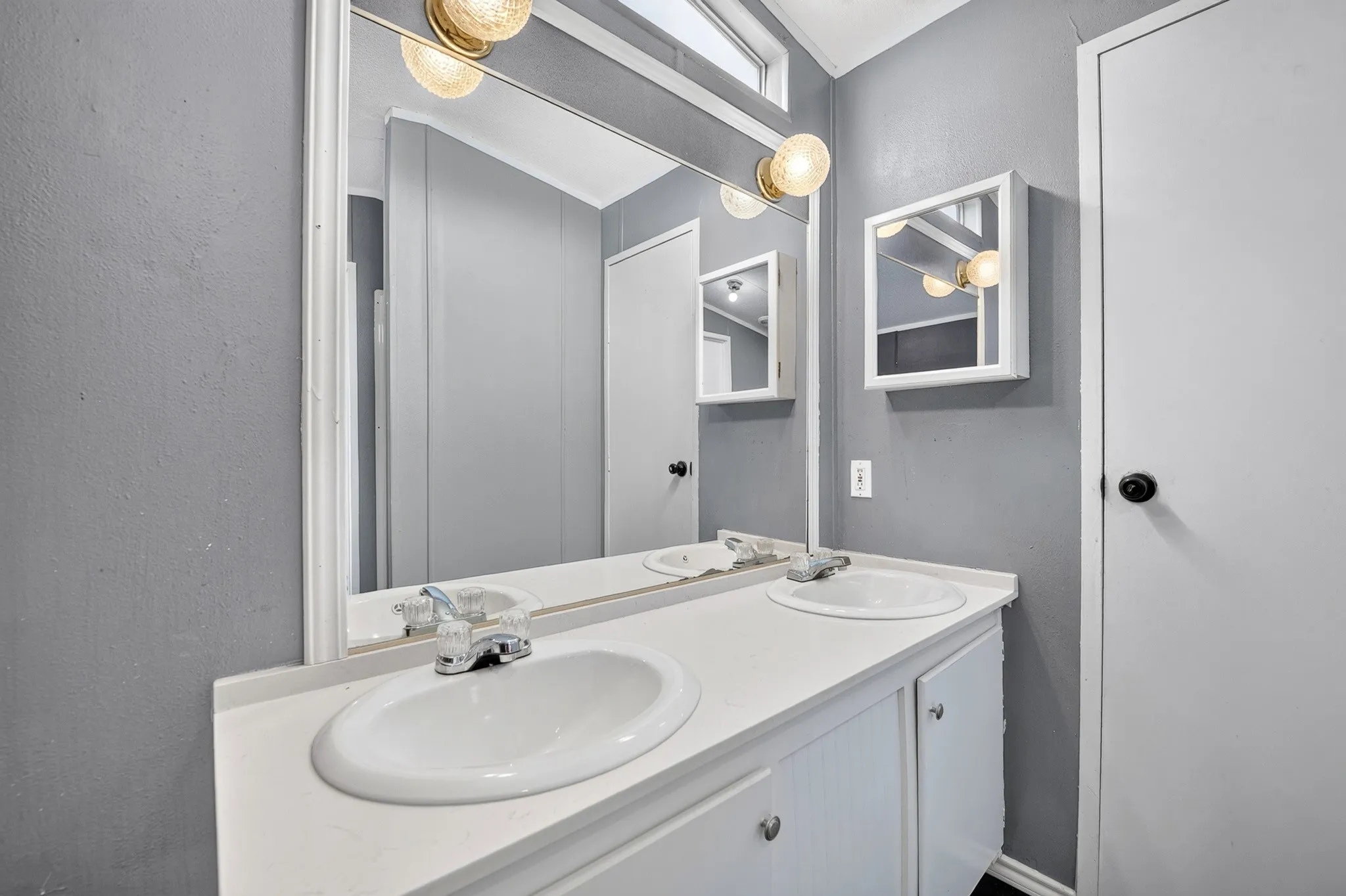 Dual-sink vanity with a solid-surface countertop, white cabinetry, large wall-mounted mirror, and two recessed medicine cabinets