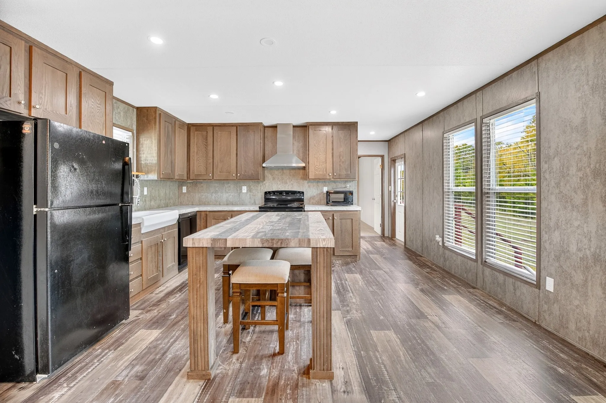 Kitchen featuring wood-finish cabinetry, stone-texture countertop island, wood-finish flooring, stainless steel range hood, and farmhouse-style apron sink