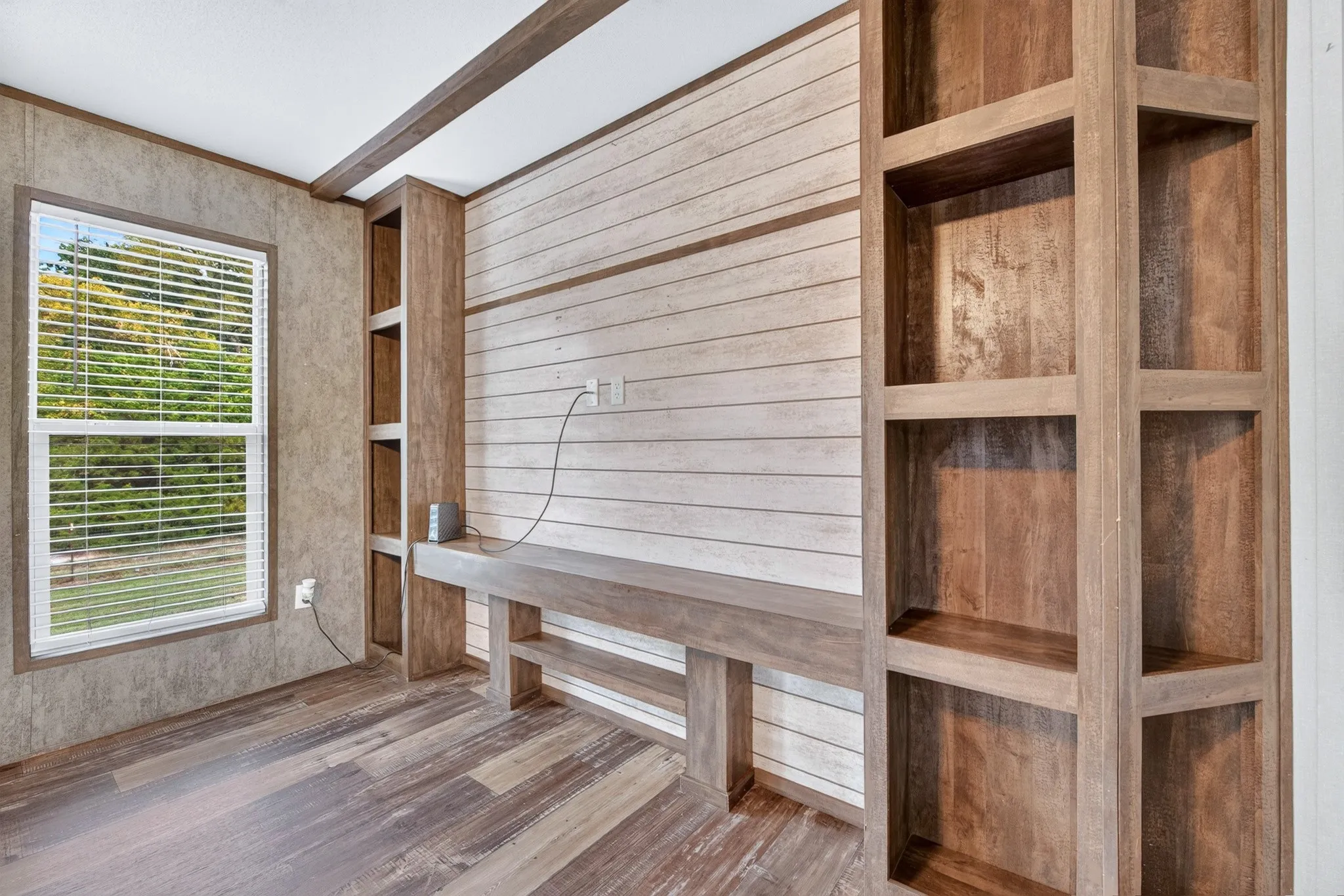 Wood-finish flooring, horizontal shiplap wall accent, and integrated built-in wood shelving featuring an expansive console counter and overhead beam detailing