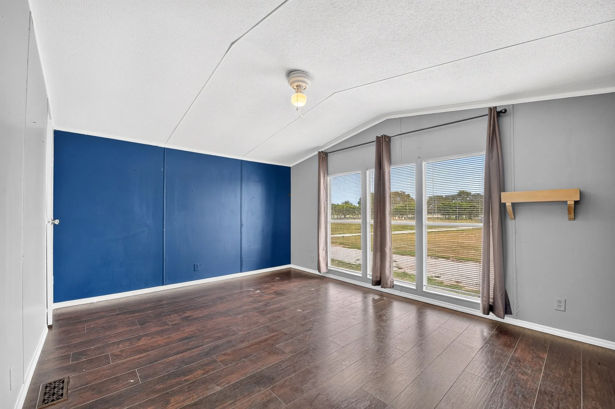 Sloped ceiling featuring a flush-mount light fixture, wood-finish flooring, and a bank of three large windows