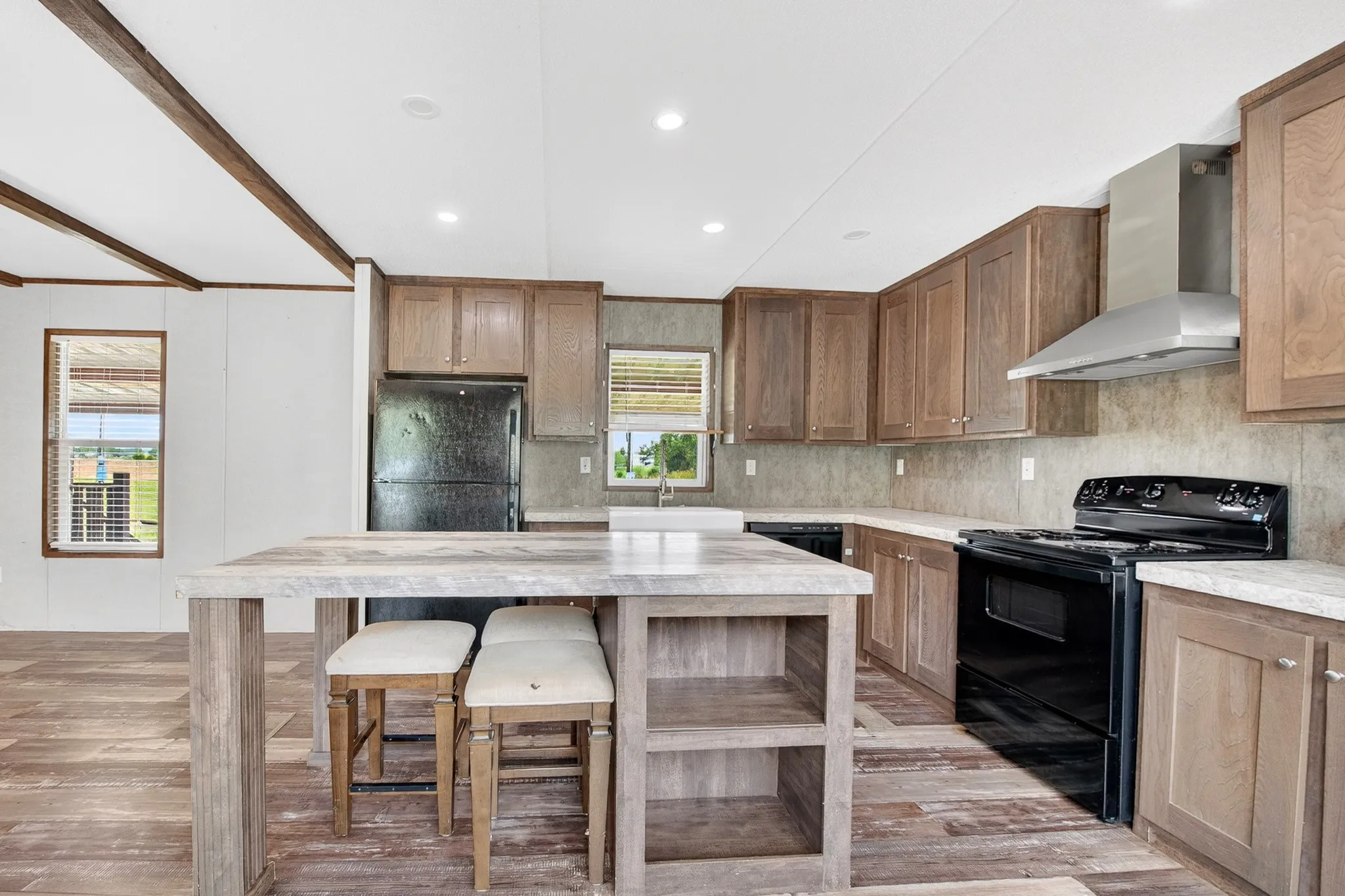 Kitchen featuring wood-finish cabinetry, a stone-patterned countertop island with built-in storage, a stainless steel range hood, and a farmhouse-style apron sink