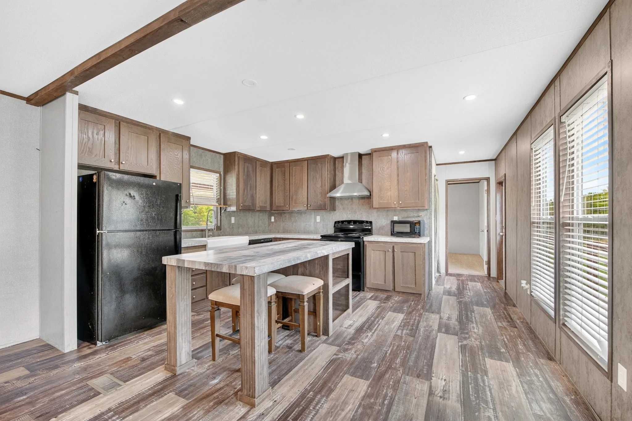 Kitchen featuring wood-finish cabinetry, a stationary kitchen island with wood-finish base, stainless steel range hood, recessed lighting, and wood-finish flooring