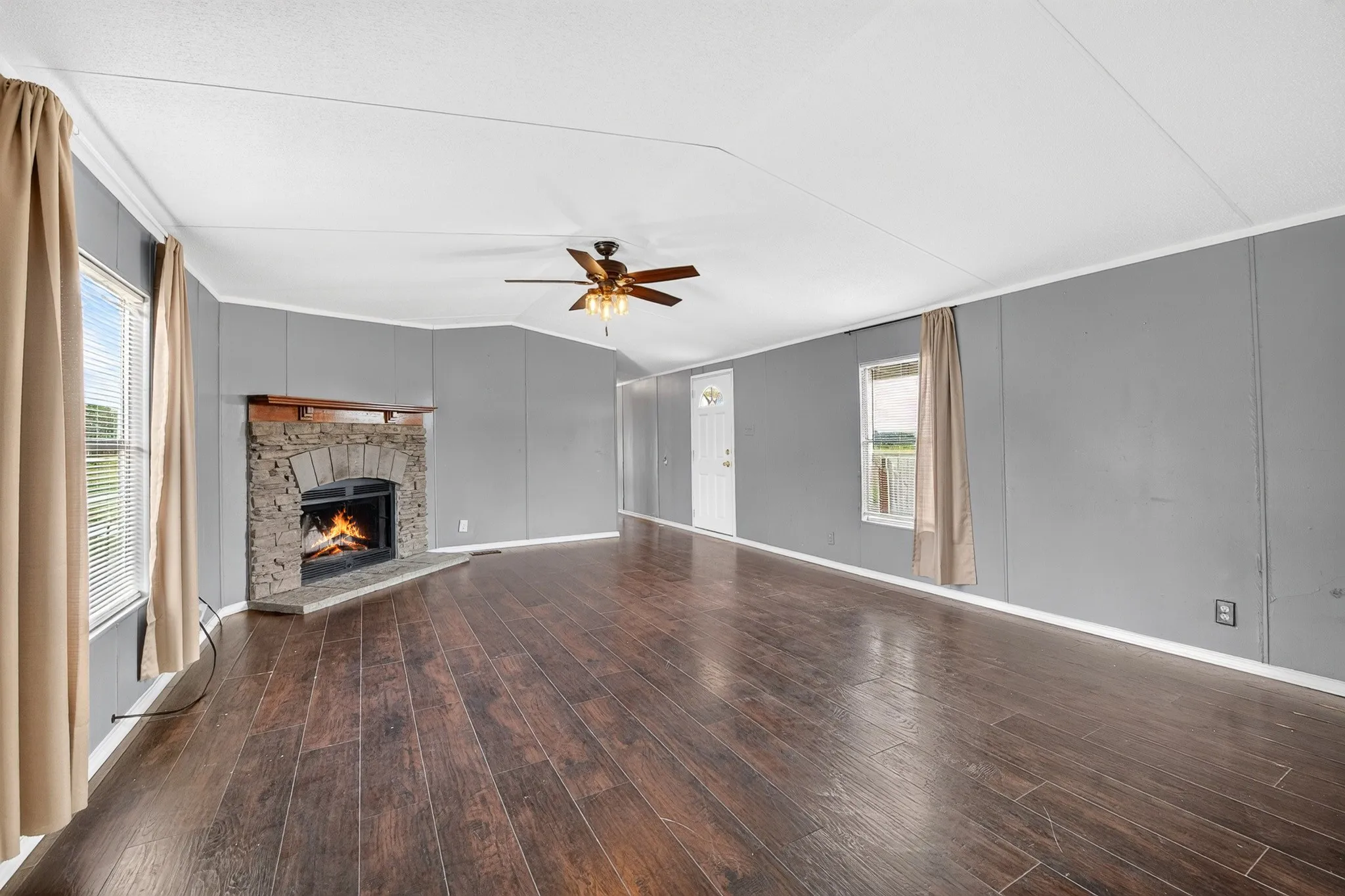 Living area featuring wood-finish flooring, a stone-surround fireplace with a timber mantel, and a ceiling fan with integrated lighting