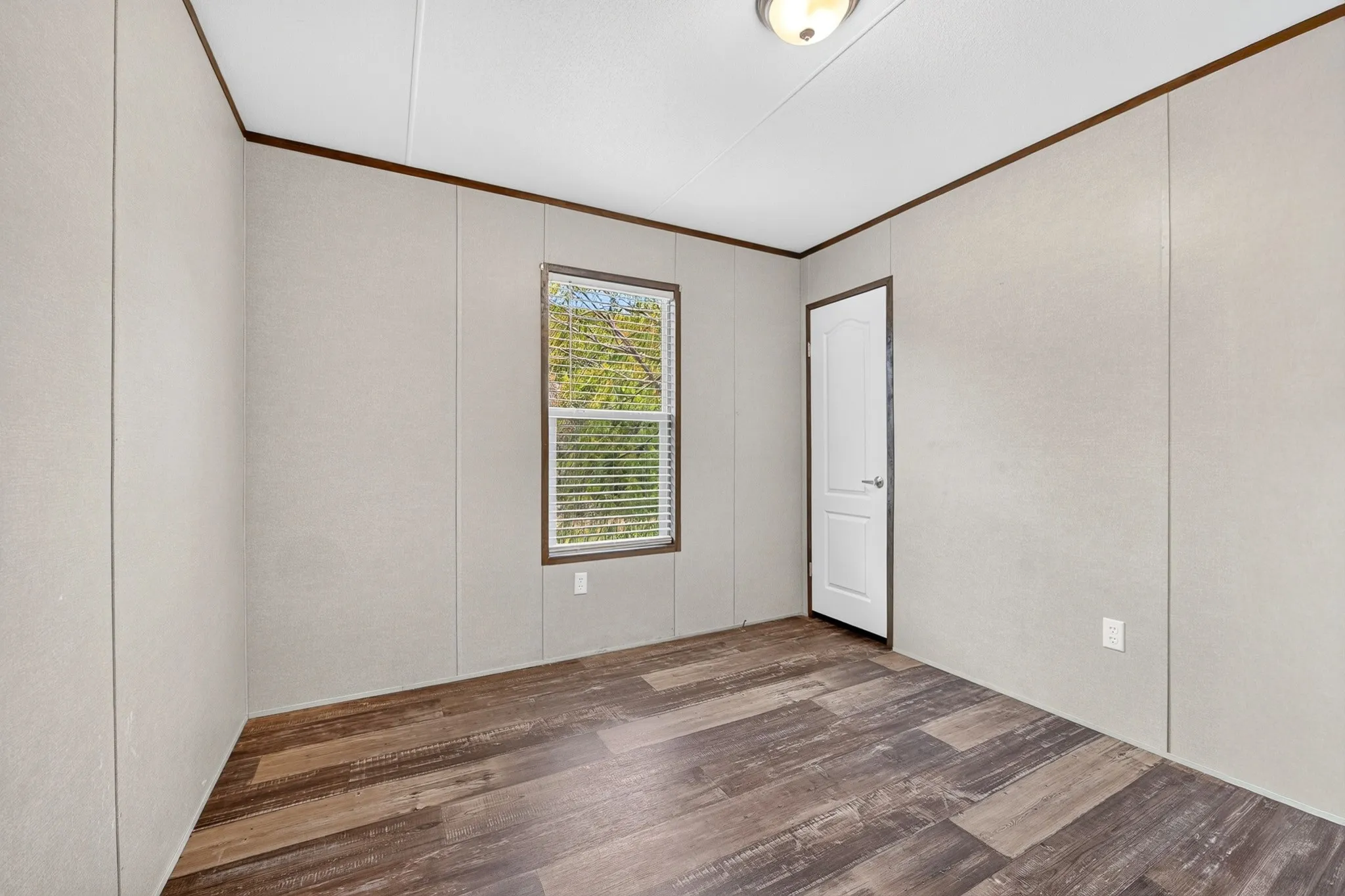 Interior space featuring wood-finish flooring, neutral wall paneling, a single-panel interior door, and a central window with blinds