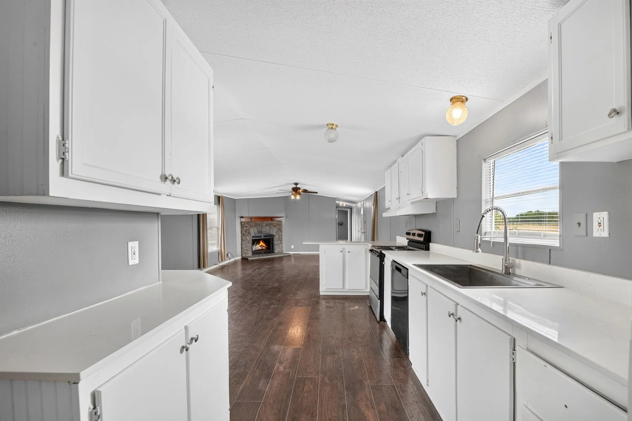 Kitchen featuring white cabinetry, solid-surface countertops, and wood-finish flooring, with a stone-surround fireplace visible in the distance