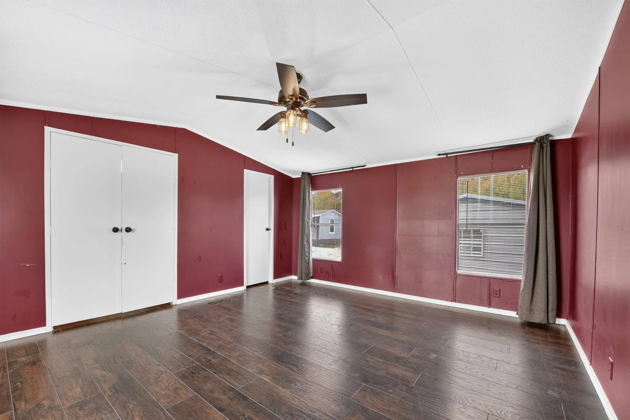 Vaulted ceiling featuring a central multi-light fan, dark wood-finish flooring, and double-door storage cabinetry
