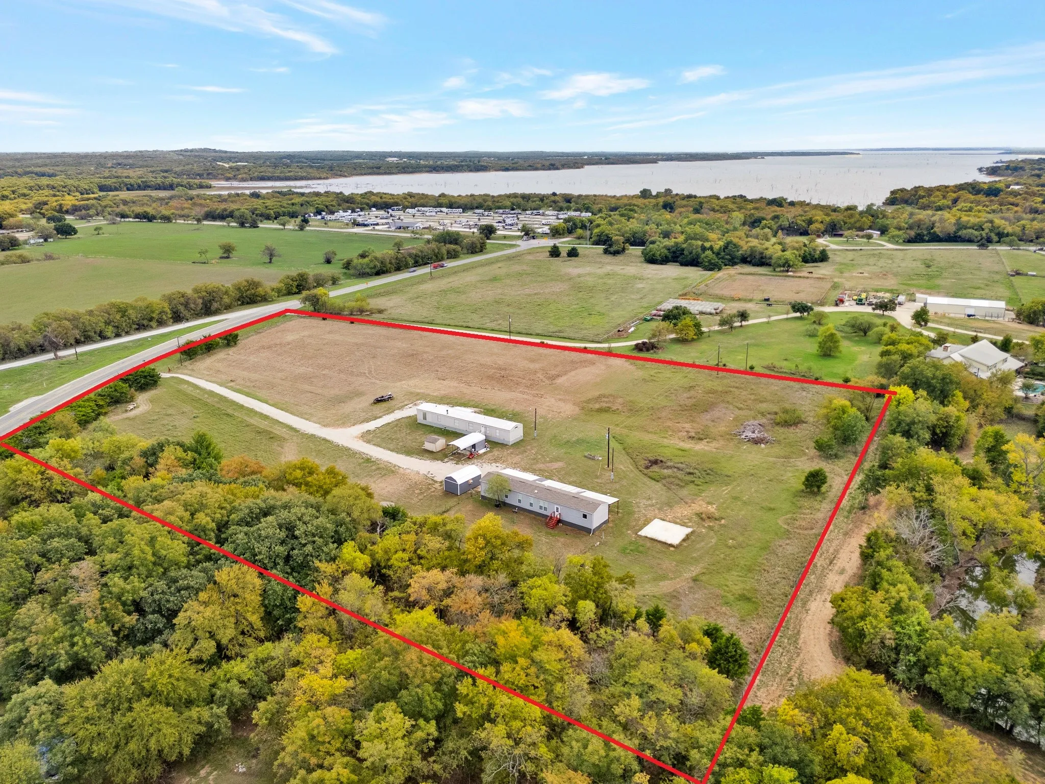 Expansive acreage featuring a gravel driveway, multiple structures, open pastureland, and mature perimeter trees