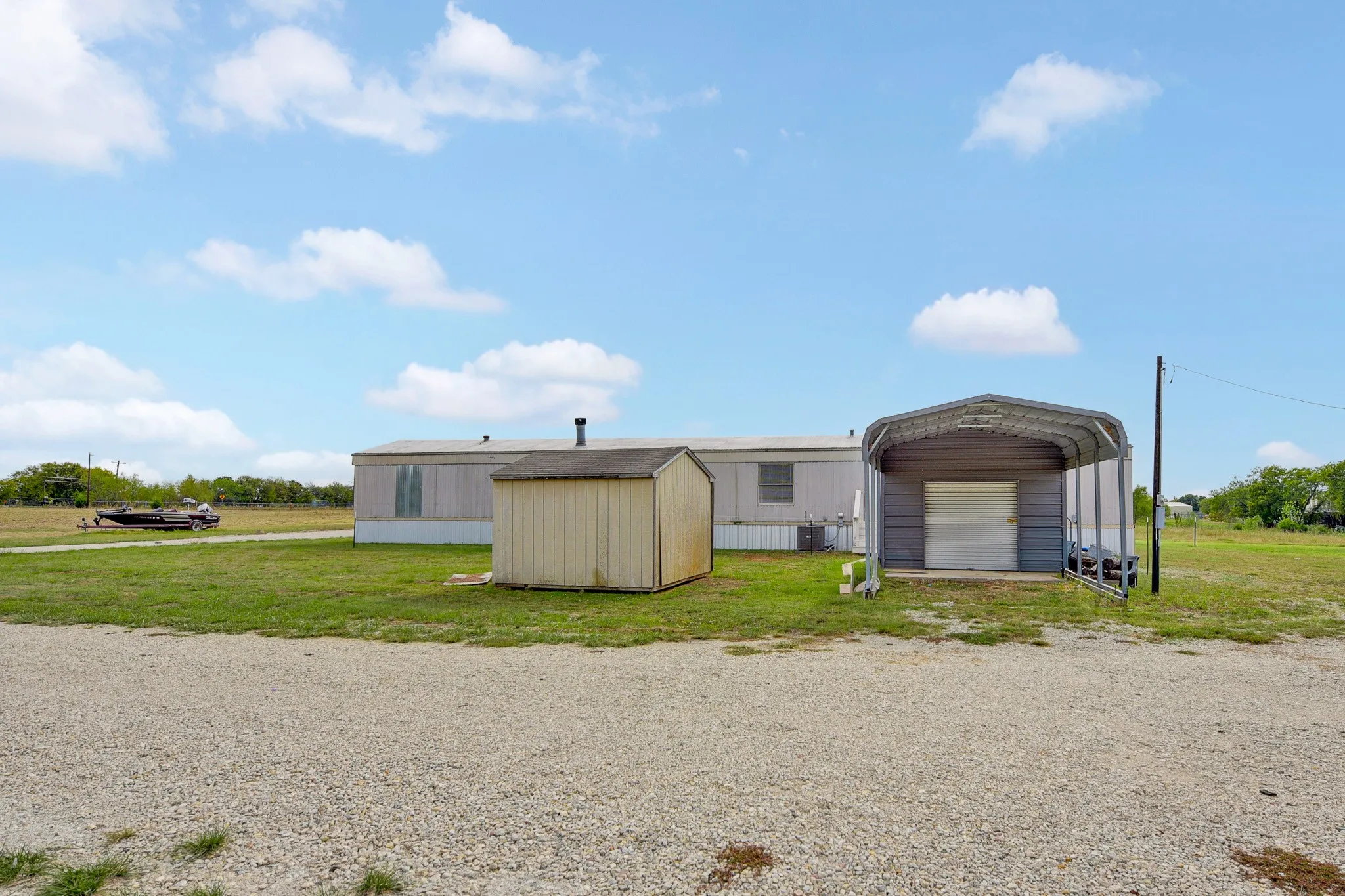 Guest House -Expansive acreage featuring a metal-frame carport, detached storage structure, and gravel driveway