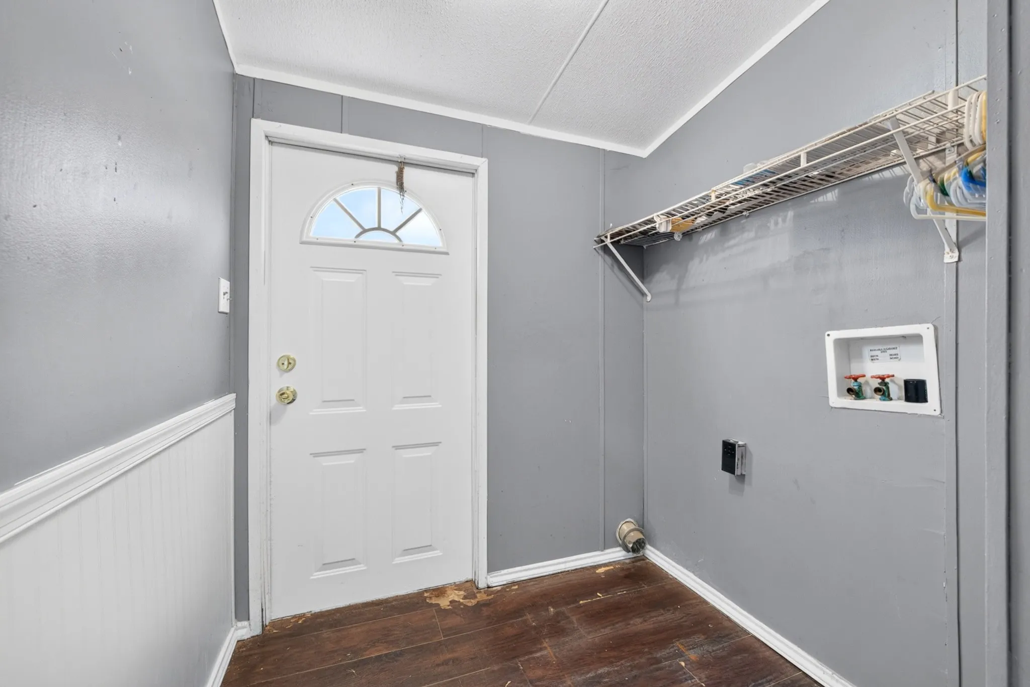 Utility area featuring wood-finish flooring, wainscoting, a wall-mounted wire storage shelf, and dedicated laundry hookups with an exterior door featuring a half-moon window