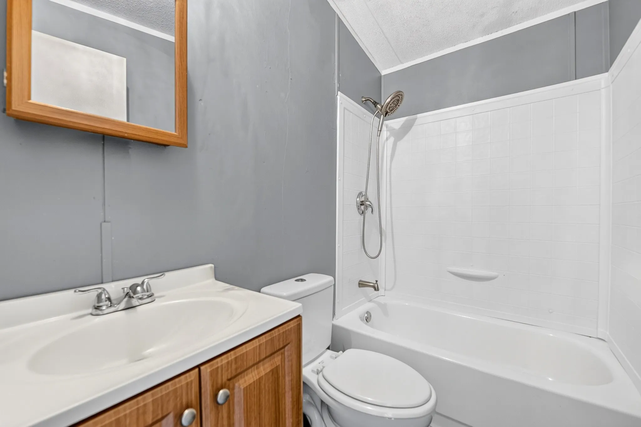 Bathroom featuring a wood-finish vanity with an integrated basin, wall-mounted medicine cabinet, and a bathtub with a shower surround and handheld sprayer