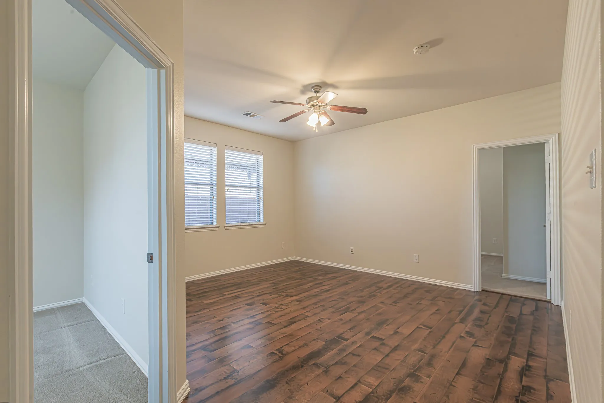 Room featuring wood-finish flooring, dual windows with blinds, a ceiling fan with light fixture, and neutral wall tones