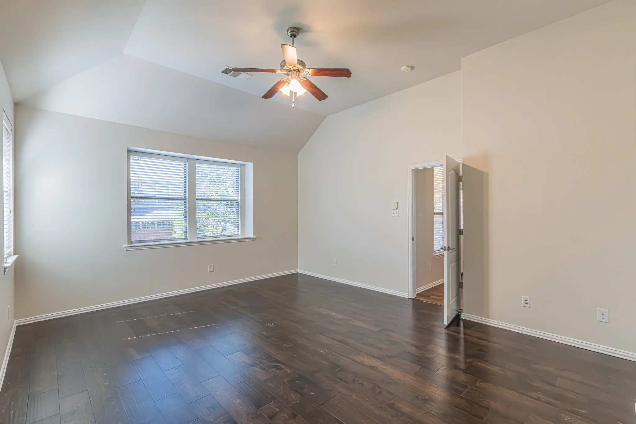 Vaulted ceiling with an integrated multi-blade ceiling fan and wood-finish flooring