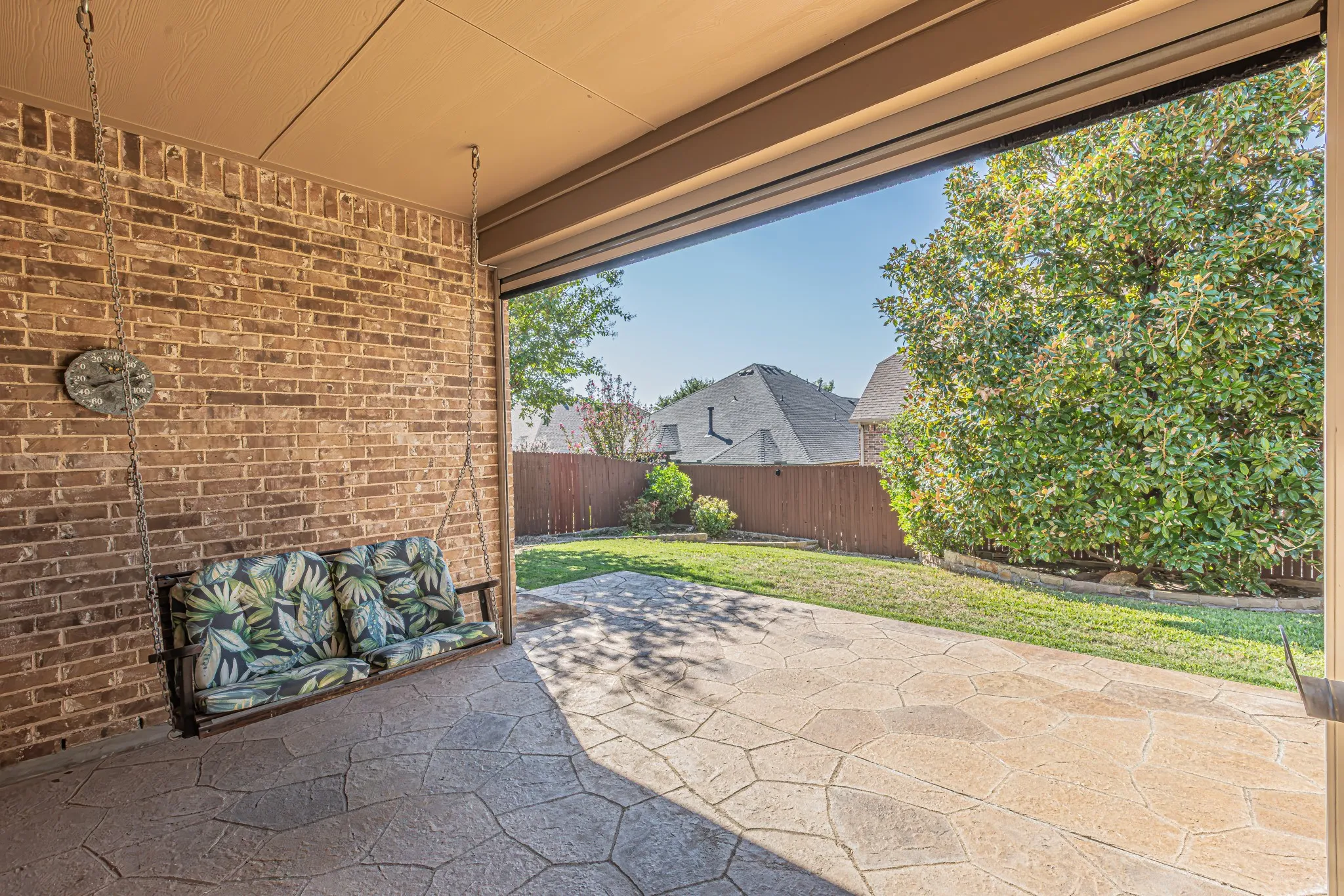 Covered patio with stamped concrete flooring, brick wall exterior, and backyard featuring a manicured lawn and wood privacy fencing