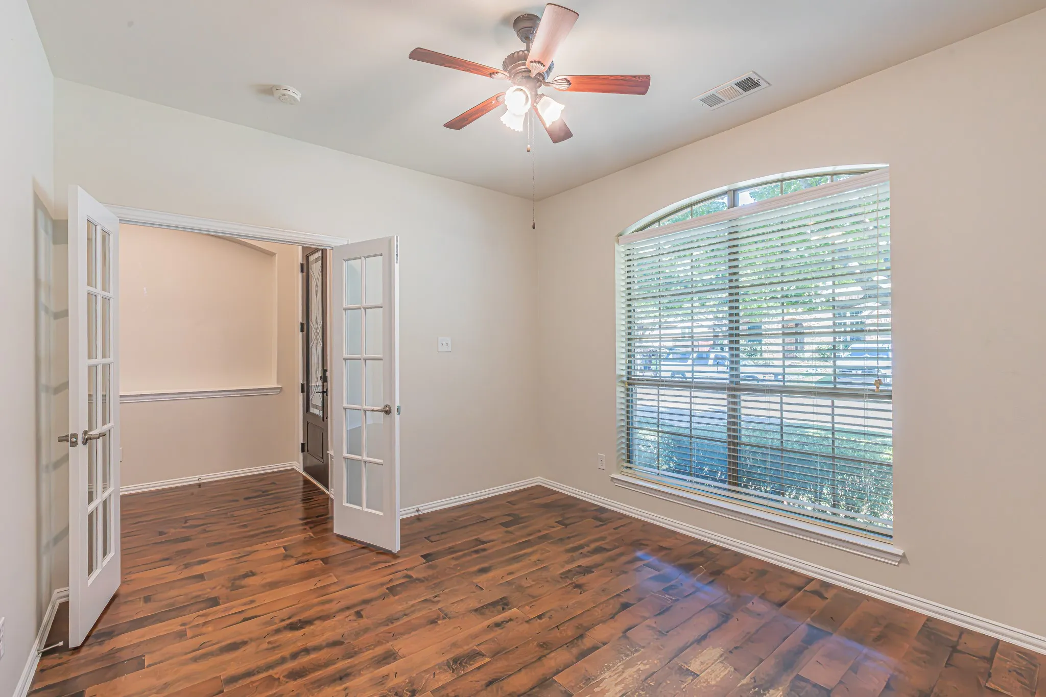 Room featuring wood-finish flooring, French doors with glass panes, an arched window, and a ceiling fan with integrated lighting. Closet, also!