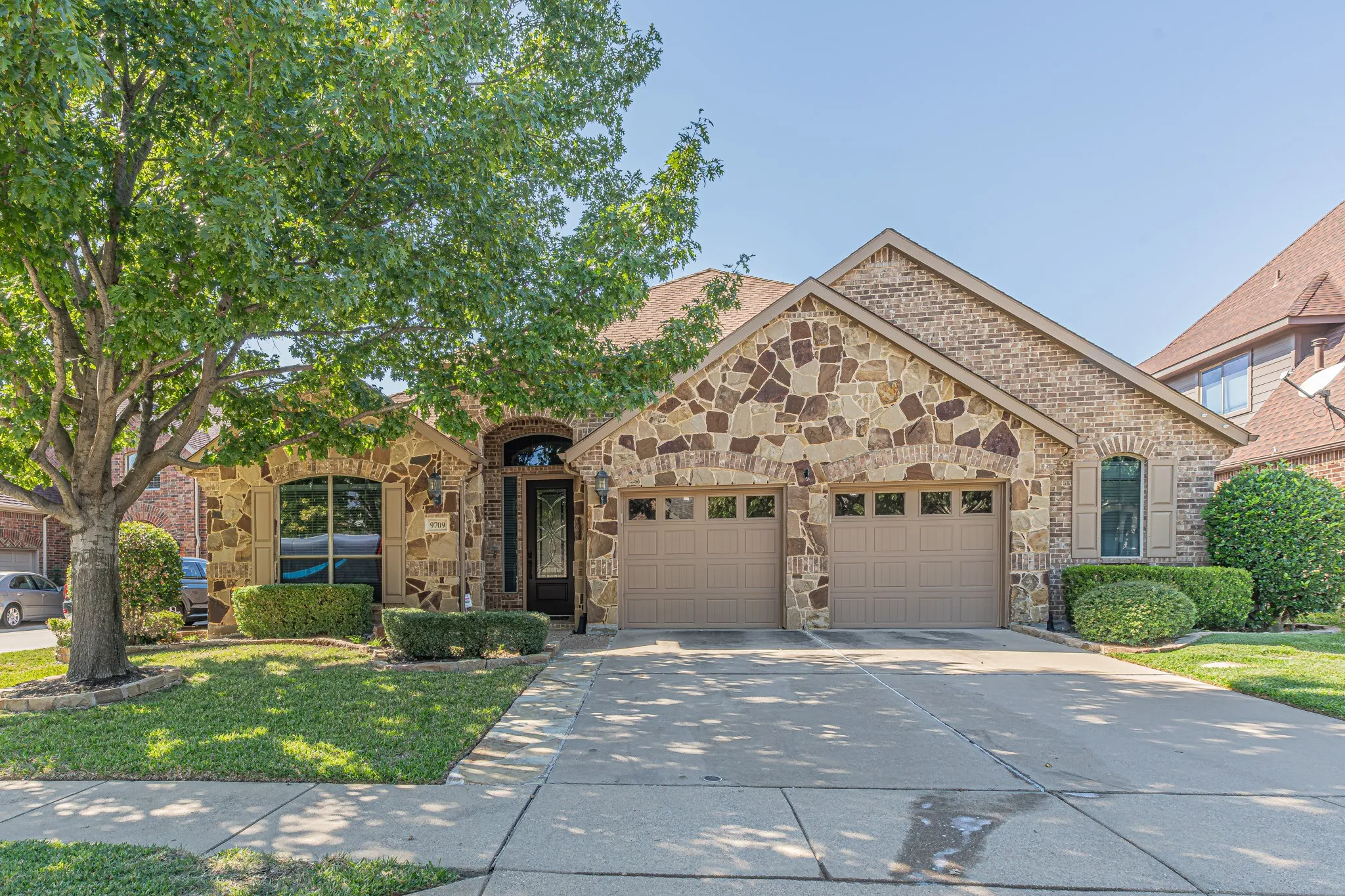 Exterior facade featuring a combination of brick and natural stone masonry, an arched entryway, and an oversized two-car garage