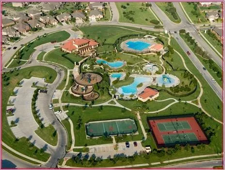 Aerial perspective of a community recreation center featuring multiple swimming pools, tennis courts, a sports court, a playground, and dedicated parking areas
