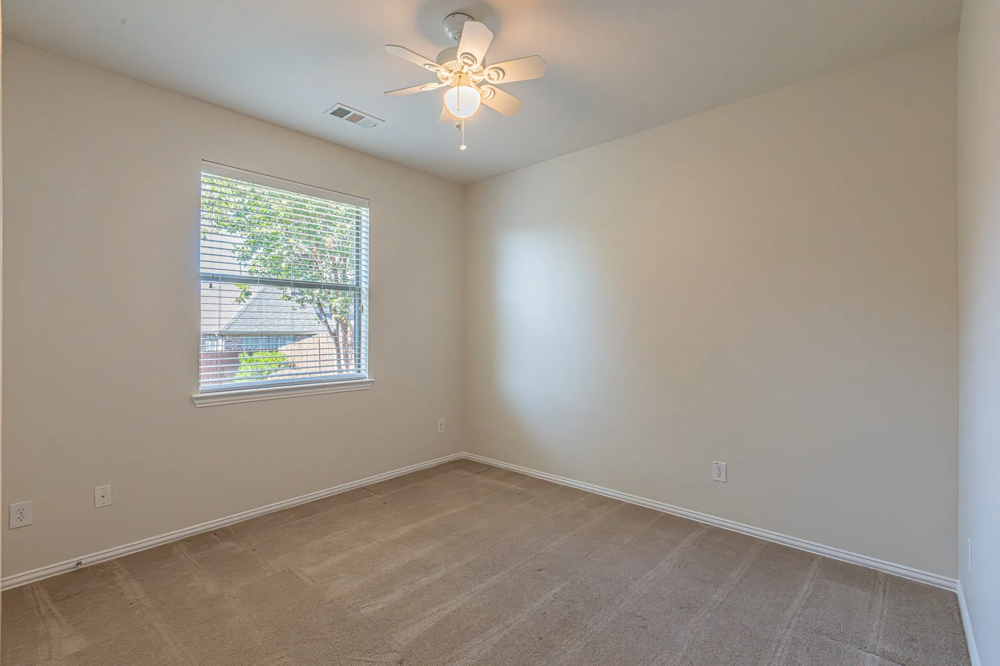 Neutral-toned interior space featuring wall-to-wall carpeting, a single-pane window with horizontal blinds, and a central ceiling fan with an integrated light fixture