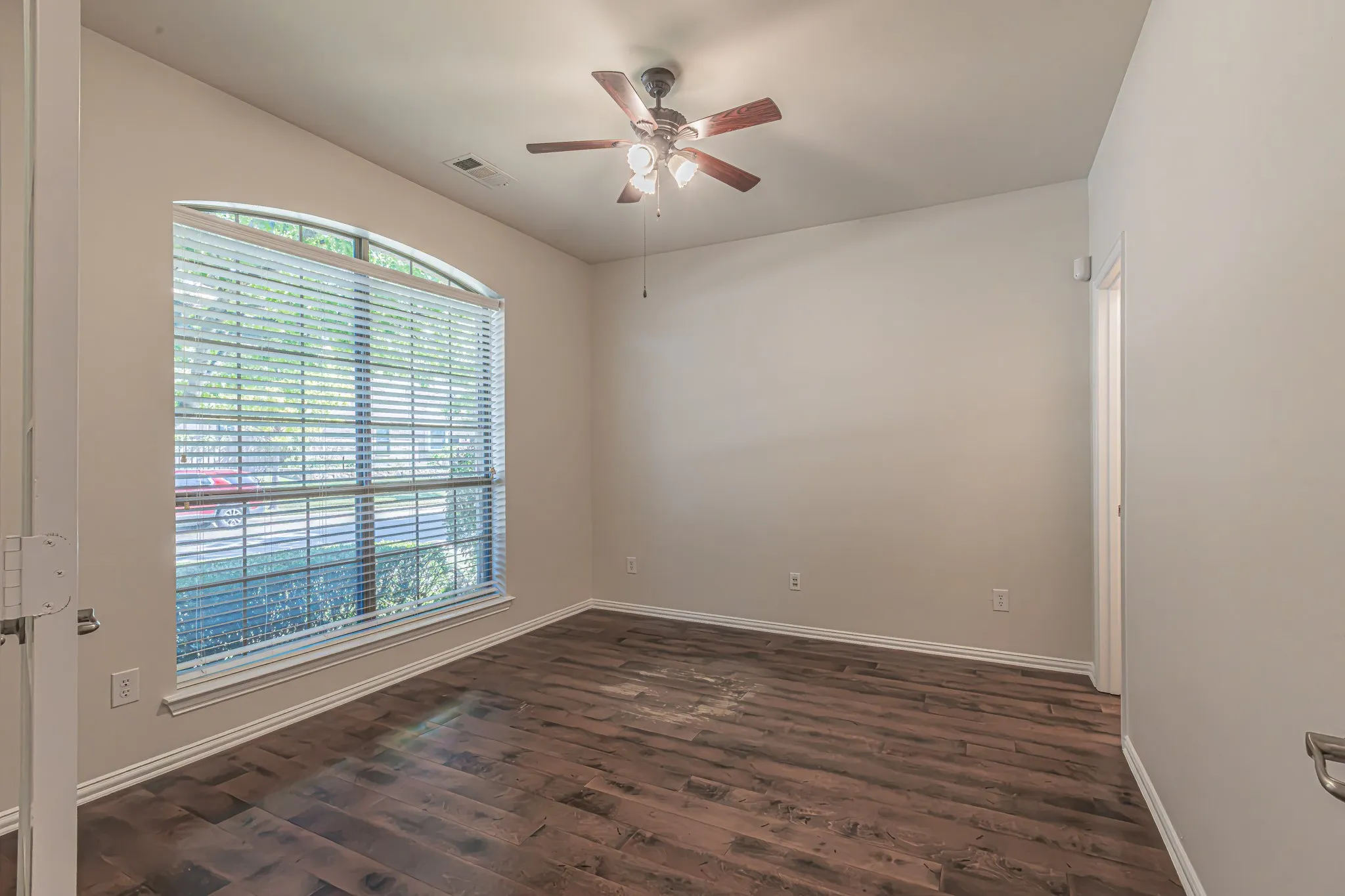 Room featuring wood-finish flooring, an arched window with horizontal blinds, and a multi-blade ceiling fan with an integrated light fixture