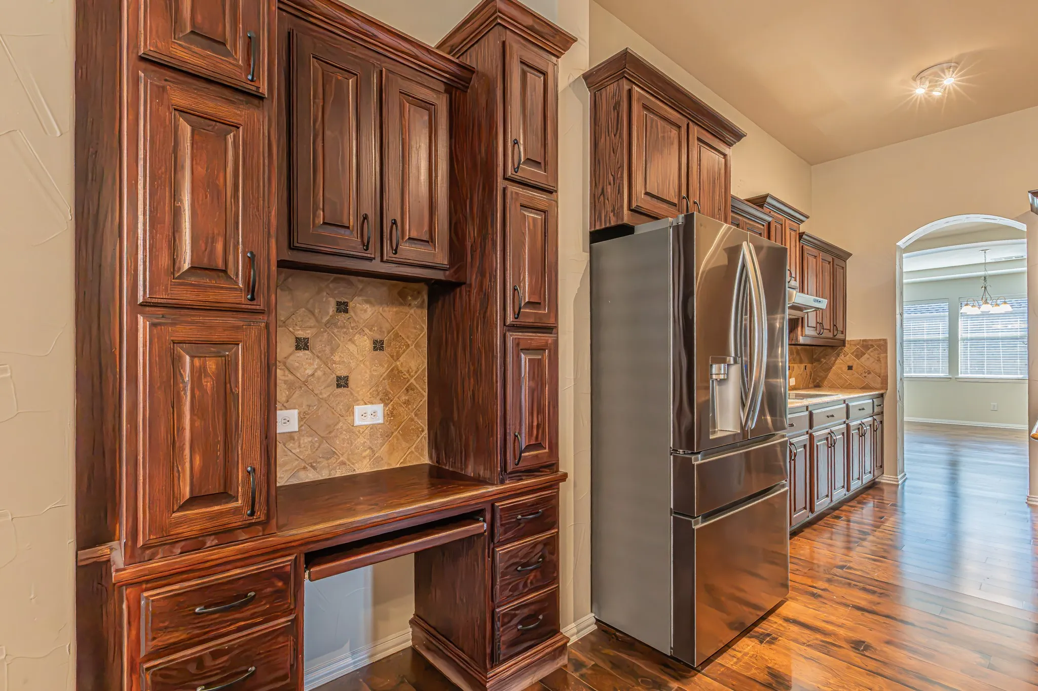 Custom built-in cabinetry with integrated desk space, decorative stone tile backsplash, stainless steel refrigerator, and wood-finish flooring