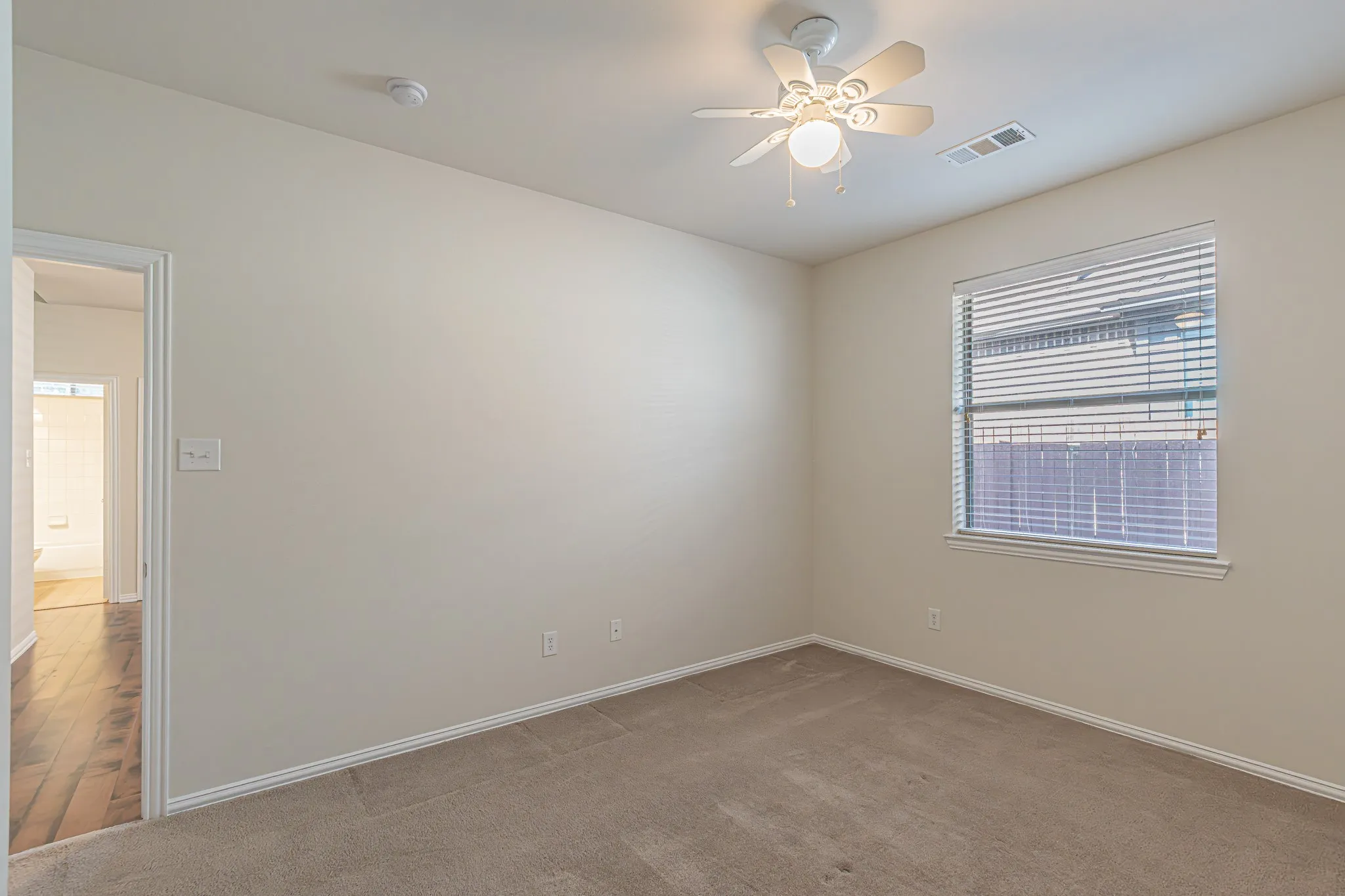 Neutral-toned wall paint, carpeted flooring, multi-blade ceiling fan with integrated lighting, and window with horizontal blinds